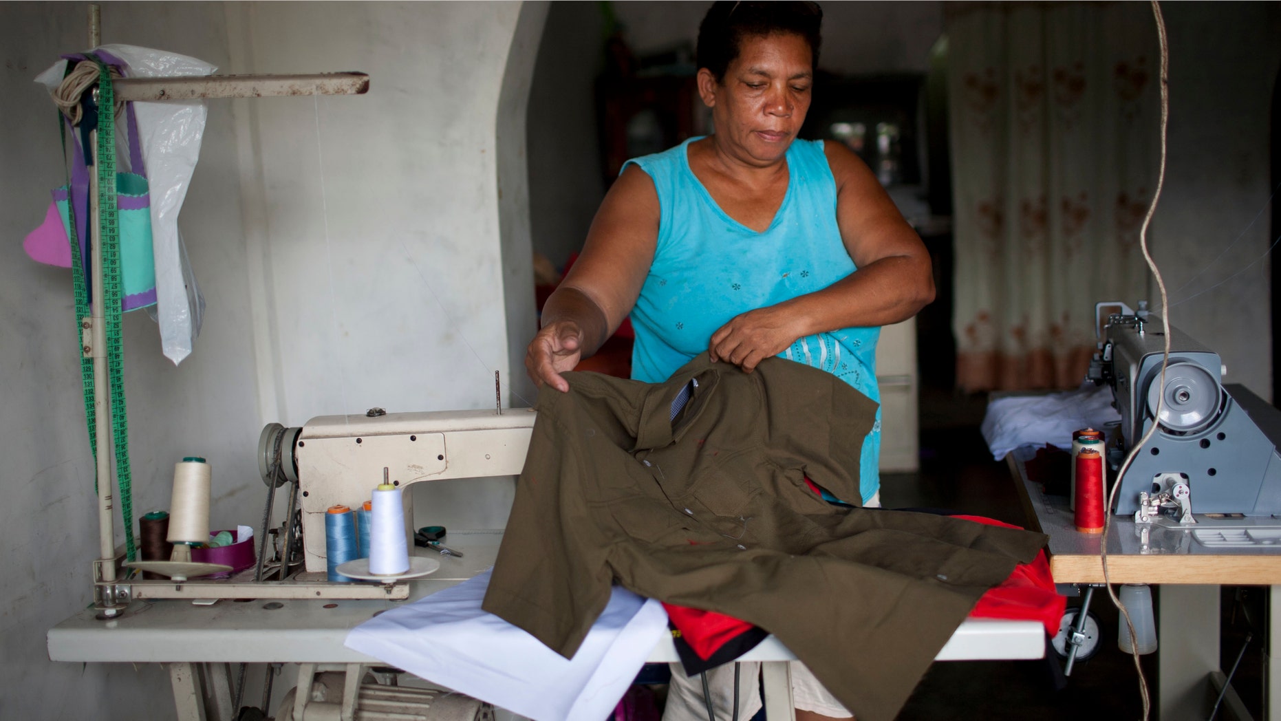 In this May 31, 2012 photo, Petra Maria Rengifo displays a shirt she sewed as she works from her home in Legon, a neighborhood built along a highway in the countryside east of Caracas, Venezuela. One of the shirts made by the business that Rengifo supplies was picked up by an aide to opposition presidential hopeful Henrique Capriles. Now, Capriles wears almost nothing but Rengifo's short-sleeved, collared shirts on the campaign trail. In fact, the garments she sews have become so popular among the candidateâs supporters that theyâre now called âthe Capriles shirt.â Venezuela will hold elections in October. (AP Photo/Ariana Cubillos)