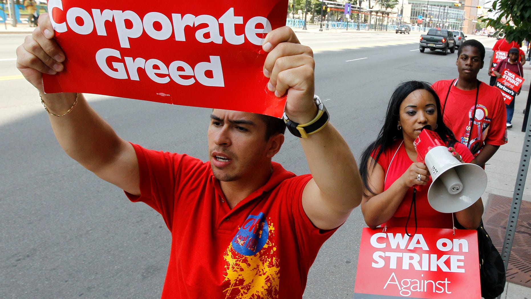 Ferdinand Hernandez, left, a sales associate who works for Verizon in Newark, N.J., holds a sign as he and coworker Leyda Jimenez, center, a multilingual consultant, picket outside of a Verizon store, Monday, Aug. 8, 2011, in Newark, N.J.