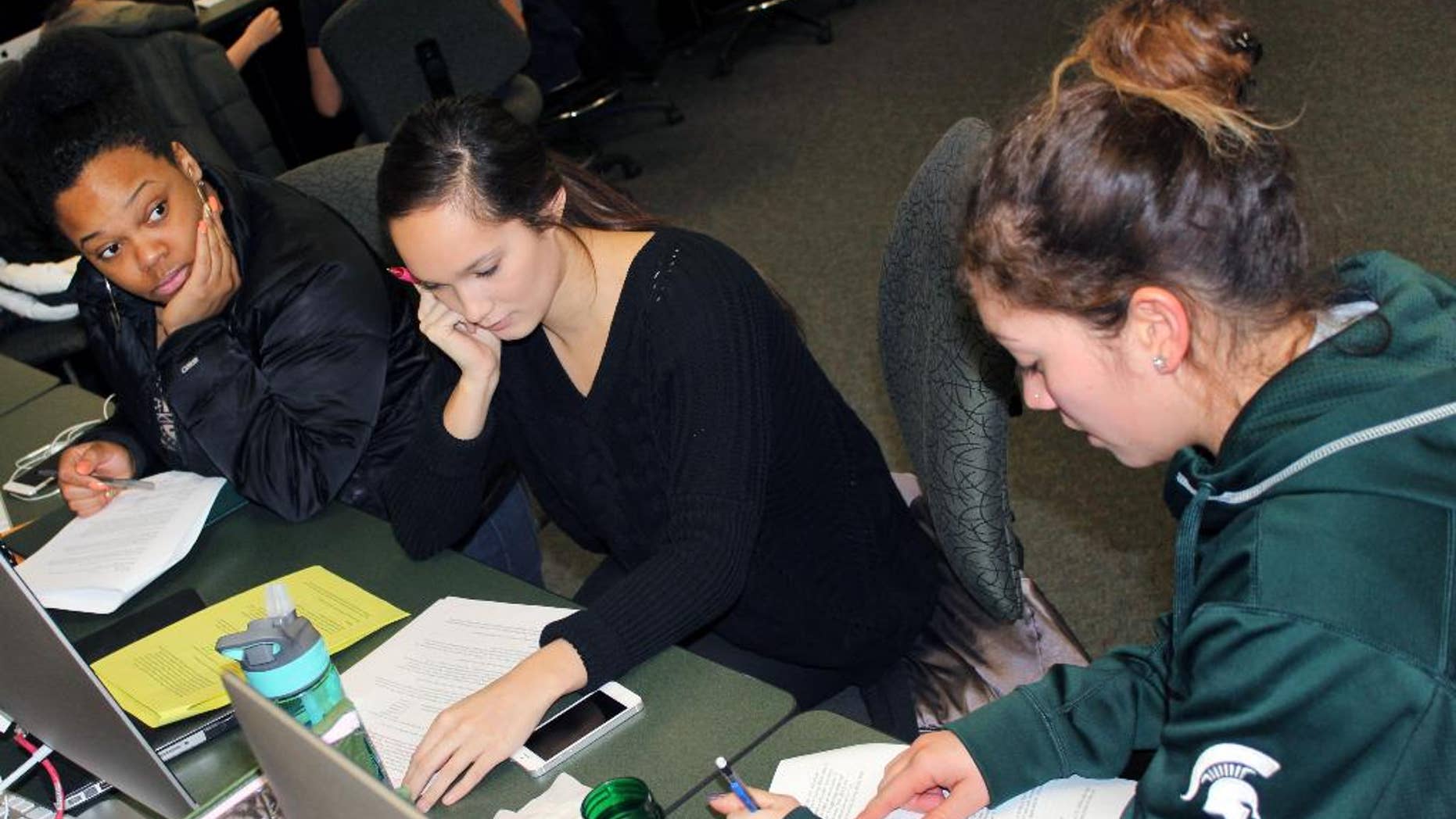In this March 1, 2015 photo released by Joe Grimm, Michigan State University students Tiara Jones, from left, Madeline Carino and Lia Kamana work on a new book “100 Questions and Answers About Veterans” in East Lansing, Mich. The new book, researched and written by a Michigan State journalism class with assistance from former servicemen and women, is aimed at clearing up myths and misunderstandings held by some civilians. (AP Photo/Joe Grimm)