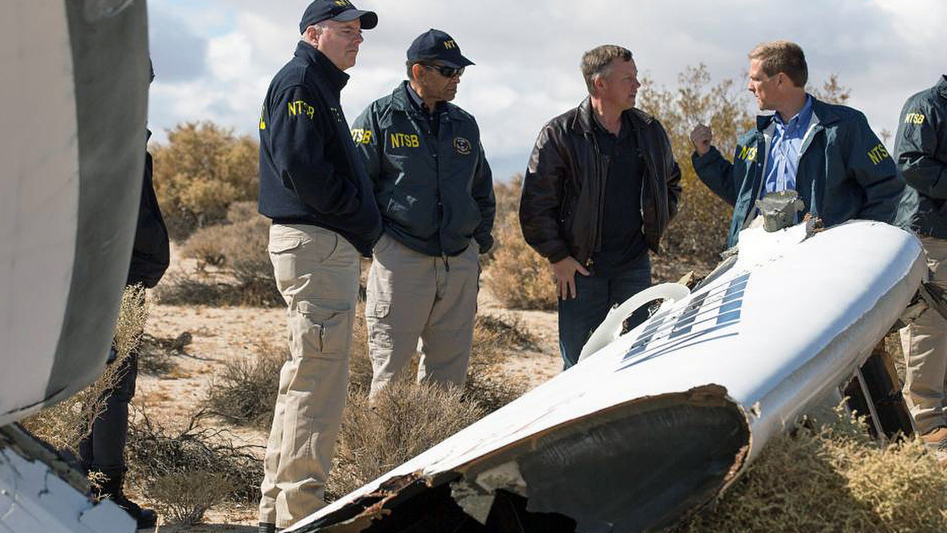 In this Nov. 1, 2014, photo provided by the National Transportation Safety Board, Virgin Galactic pilot Todd Ericson, right, talks with NTSB Acting Chairman Christopher A. Hart, second from left, at the SpaceShipTwo accident site with investigators in Mojave, Calif. The cause of Friday's crash of Virgin Galactic's SpaceShipTwo has not been determined, but investigators found the "feathering" system, which rotates the tail to create drag, was activated before the craft reached the appropriate speed, National Transportation Safety Board Acting Chairman Christopher Hart said. (AP Photo/NTSB)