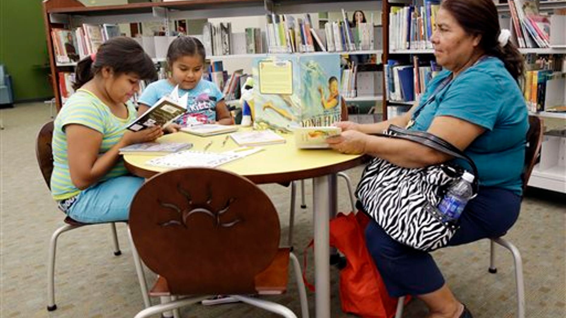 In this Friday, July 19, 2013 photo, Maria Lopez, right, reads in the city library alongside daughters Emily, 9, at left, and Esmeralda, 7, in Watsonville, Calif. In the bricked plaza, strolling musicians wearing glitzy cowboy outfits blast a mariachi song, while Spanish-speaking shoppers bustle between farm stands choosing tasty cactus leaves and fresh chiles. Welcome to an increasingly typical town in California, a state where Hispanics become the largest ethnic group this summer. As the Golden State becomes less and less white, communities are becoming more segregated, not less. (AP Photo/Marcio Jose Sanchez)