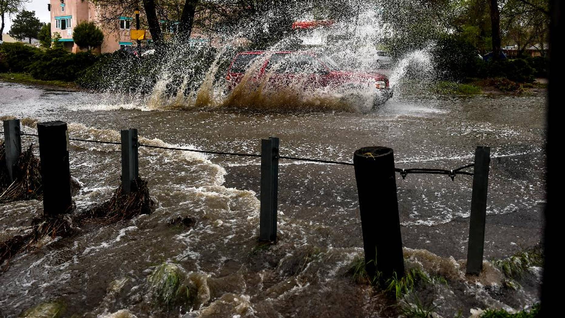 FILE - In this May 5, 2015 file photo, a car navigates a flooded intersection as a small stream empties over the road as a storm rages over Colorado Springs, Colo. While California and much of the far West are suffering through extreme drought, Colorado is splashing through a wetter-than-normal spring. (Michael Ciaglo/The Gazette via AP, file) MAGS OUT; MANDATORY CREDIT