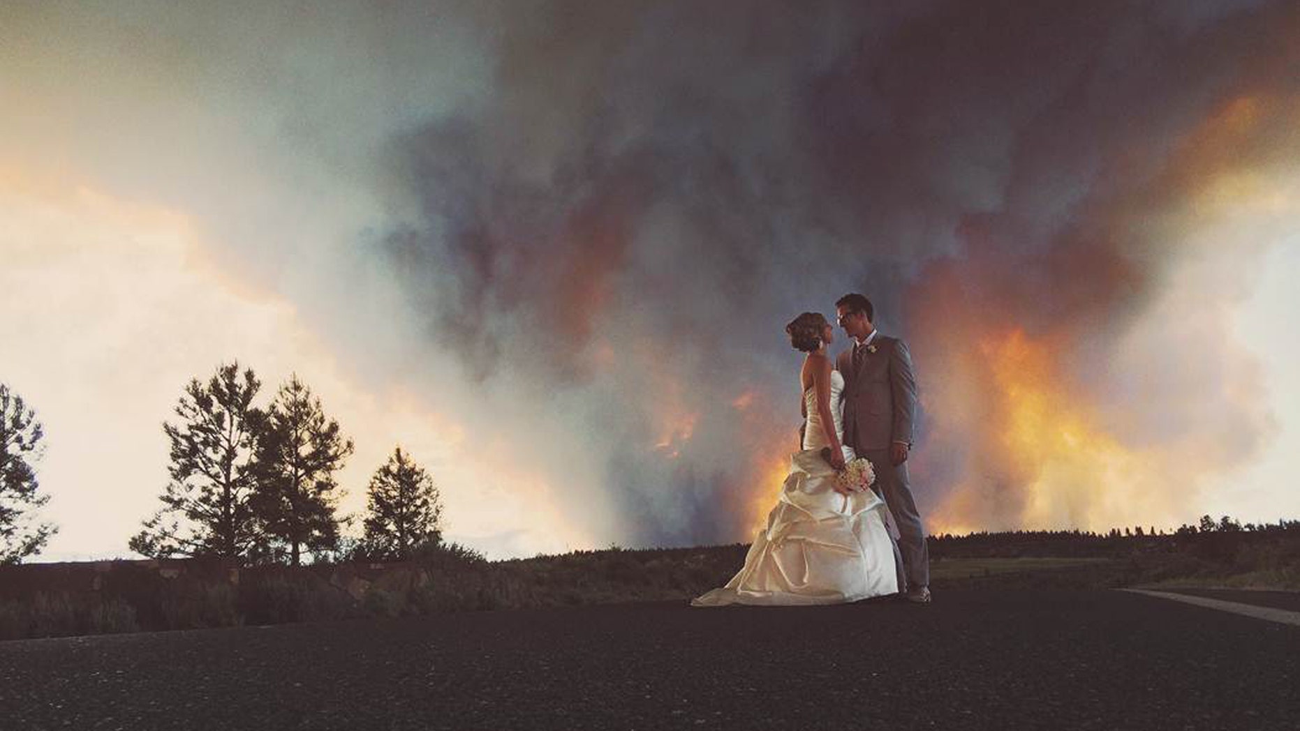 In this Saturday, June 7, 2014 photo provided by Josh Newton, newlyweds Michael Wolber and April Hartley pose for a picture near Bend, Ore., as a wildfire burns in the background. Because of the approaching fire, the minister conducted an abbreviated ceremony and the wedding party was evacuated to a downtown Bend park for the reception. (AP/Josh Newton)