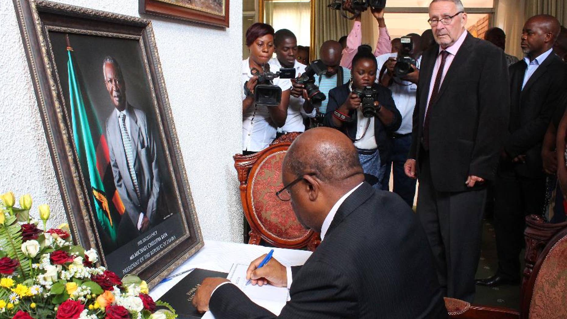 Acting Zambian president Guy Scott, second from right, watches over as eductaion minister John Phiri, foreground, signs a book of condolences in Lusaka, Friday, Oct. 31, 2014. Scott has taken over as acting president after President Michael Sata, in framed photo left, passed away in a London hospital last Sunday night. Sata's body will be returned to Lusaka, Saturday, with a state funeral planed for Nov. 11, 2014. (AP PhotoMoses Mwape)
