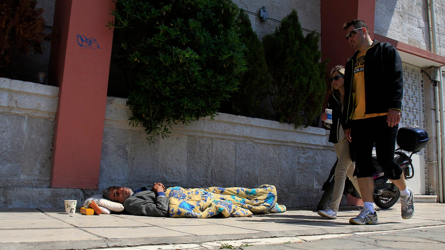 Pedestrians walk by a homeless man in Thessaloniki, Greece, Sunday, April 21. 2013. Under an international bailout deal that saved it from bankruptcy in 2010, Greece agreed to slash bloated budget deficits, repeatedly cutting pensions and salaries while hiking taxes. (AP Photo/Nikolas Giakoumidis)