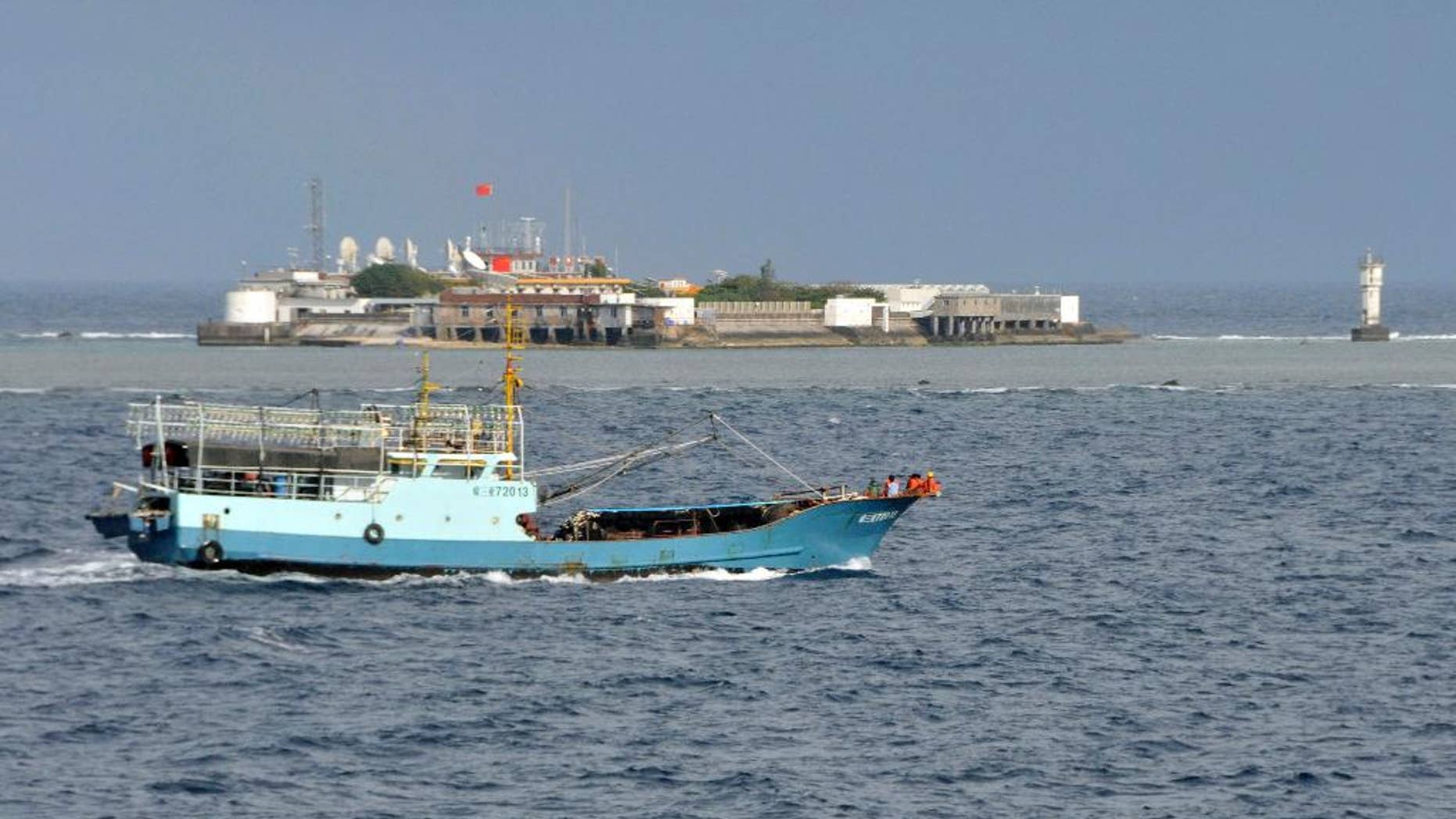 FILE - In this July 15, 2012 file photo released by China's Xinhua News Agency, a Chinese fishing vessel sails by Fiery Cross Reef, background, also known as Yongshu Reef by the Chinese, of the Spratly Islands in South China Sea. Defying a U.S. call to halt the project, China defended its land reclamation in the disputed Spratly Islands on Monday, Nov. 24, 2014, saying the work is for public service use, although a London-based security group says the new island could host a military airfield to intimidate neighbors. In a recent report, IHS Jane's said satellite images taken in August and November showed that Chinese dredgers had created a land mass almost the entire length of Fiery Cross Reef, which was previously under water. The security group said it is China's largest construction project in the island chain. (AP Photo/Xinhua, Wang Cunfu, File) NO SALES