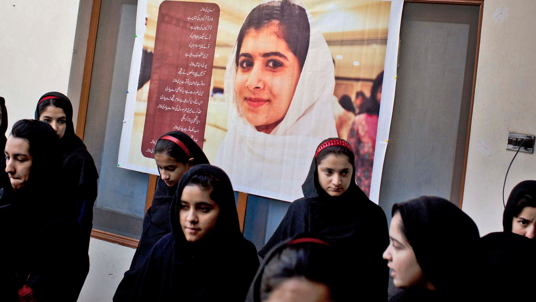 In this Thursday, Nov. 15, 2012 photo, Pakistani girls gather under a poster of Malala Yousufzai in her old school in Mingora, Swat Valley, Pakistan. The giant poster of her that once emblazoned the wall of the assembly hall has been removed. The school made no plans to recognize the anniversary of Malala's shooting by Taliban, teachers and students are afraid. (AP Photo/Anja Niedringhaus)