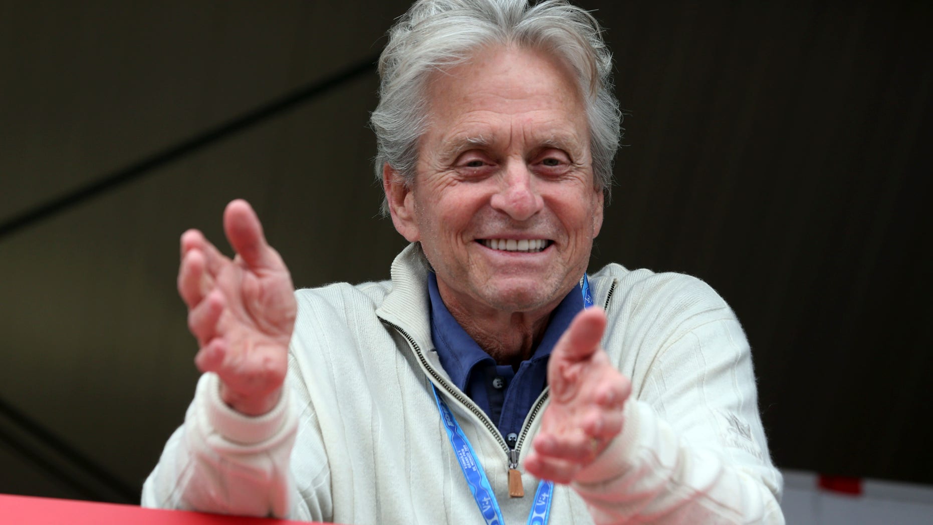 US actor Michael Douglas smiles as he watches from the Ferrari pits during the qualifying session, at the Monaco racetrack in Monaco, Saturday, May 25, 2013. The Formula one race will be held on Sunday. (AP Photo/Luca Bruno)