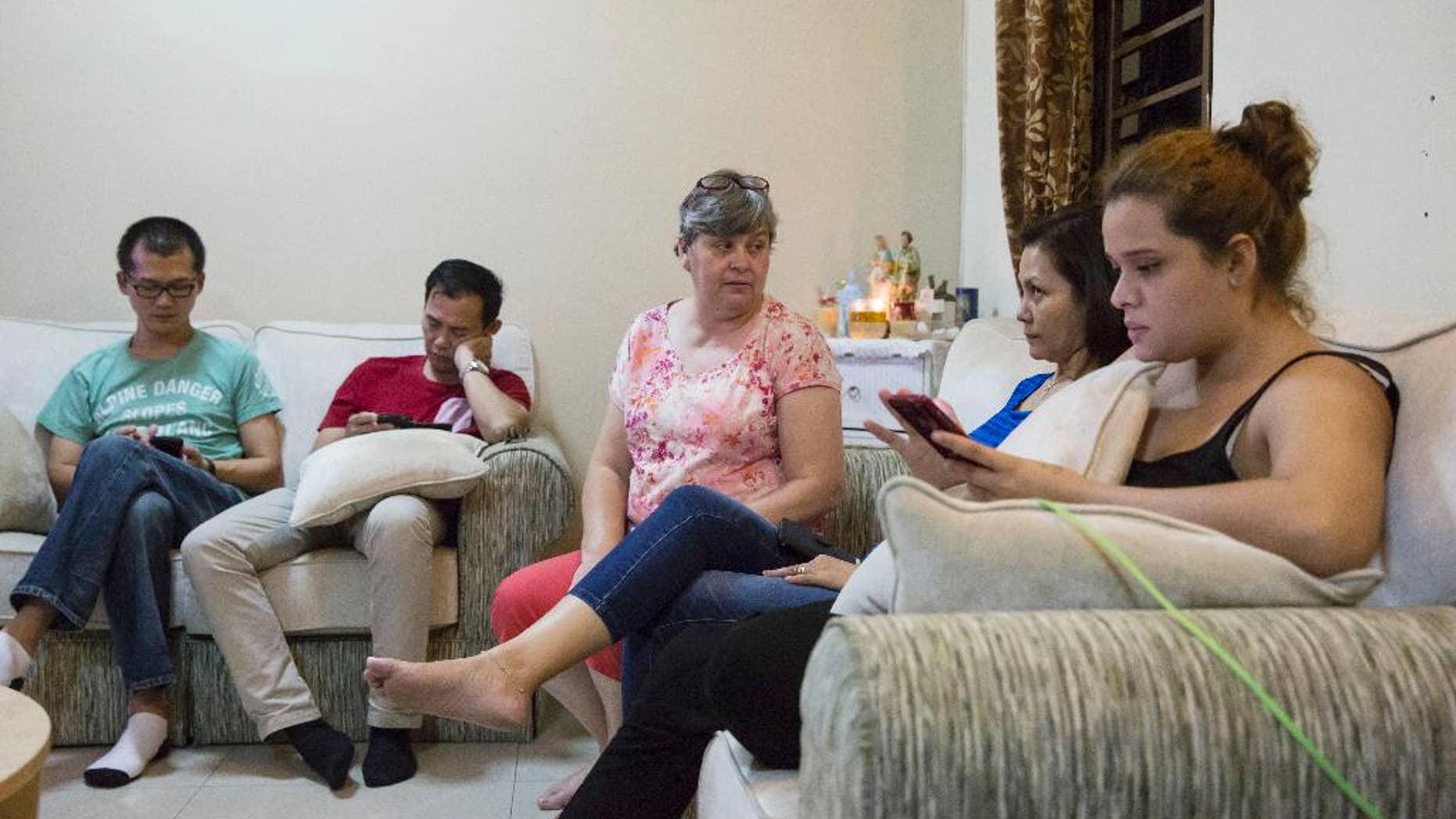 Family members of the missing on Malaysia Airlines Flight 370, from left to right: Lee Khim Fatt, husband of Foong Wai Yueng, flight attendant; Choi Loong Chow, husband of Goh Sock Lay, chief stewardess; Jacquita Gomes, wife of Patrick Gomes, in flight supervisor; and Melanie Antonio, wife to Andrew Nari, chief steward; and Nicolette Gomez, daughter of Patrick Gomes, check their mobile devices in Gomes's house outside Kuala Lumpur, Malaysia, as they wait for further news on Wednesday, Aug. 5, 2015. French and Malaysian experts on Wednesday began examining an airplane wing fragment that could offer the first tangible clue about the fate of Malaysia Airlines Flight 370, which vanished more than a year ago with 239 people aboard. (AP Photo/Joshua Paul)