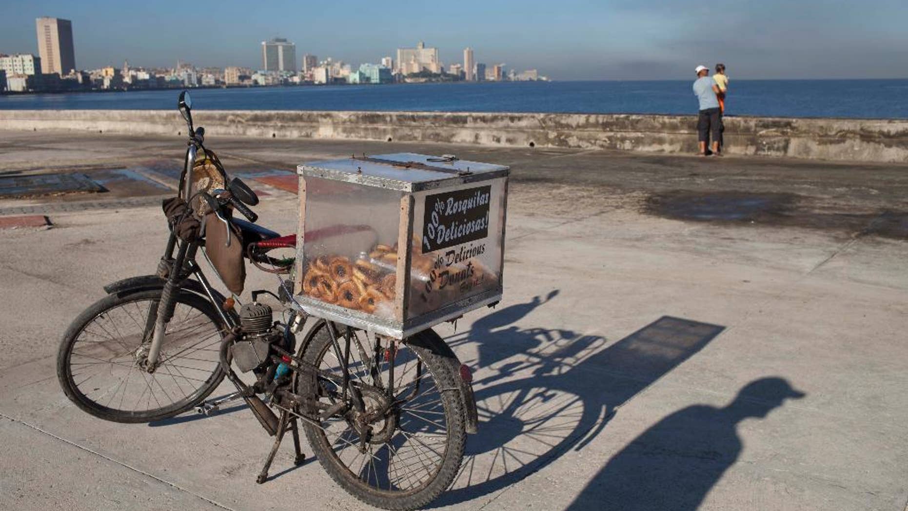 The shadow of self-employed Juan Carlos Lazo is cast on the cement next to his motorized bicycle which he uses to sell donuts along the Malecon in Havana, Cuba, early Tuesday, Oct. 28, 2014. The U.N. General Assembly is expected to vote on Tuesday to condemn the U.S. commercial, economic and financial embargo against Cuba for the 23rd year in a row. The embargo was first enacted in 1960 following Cuba's nationalization of properties belonging to U.S. citizens and corporations. Sanctions against the Caribbean nation were further strengthened to a near-total embargo in 1962. (AP Photo/Franklin Reyes)