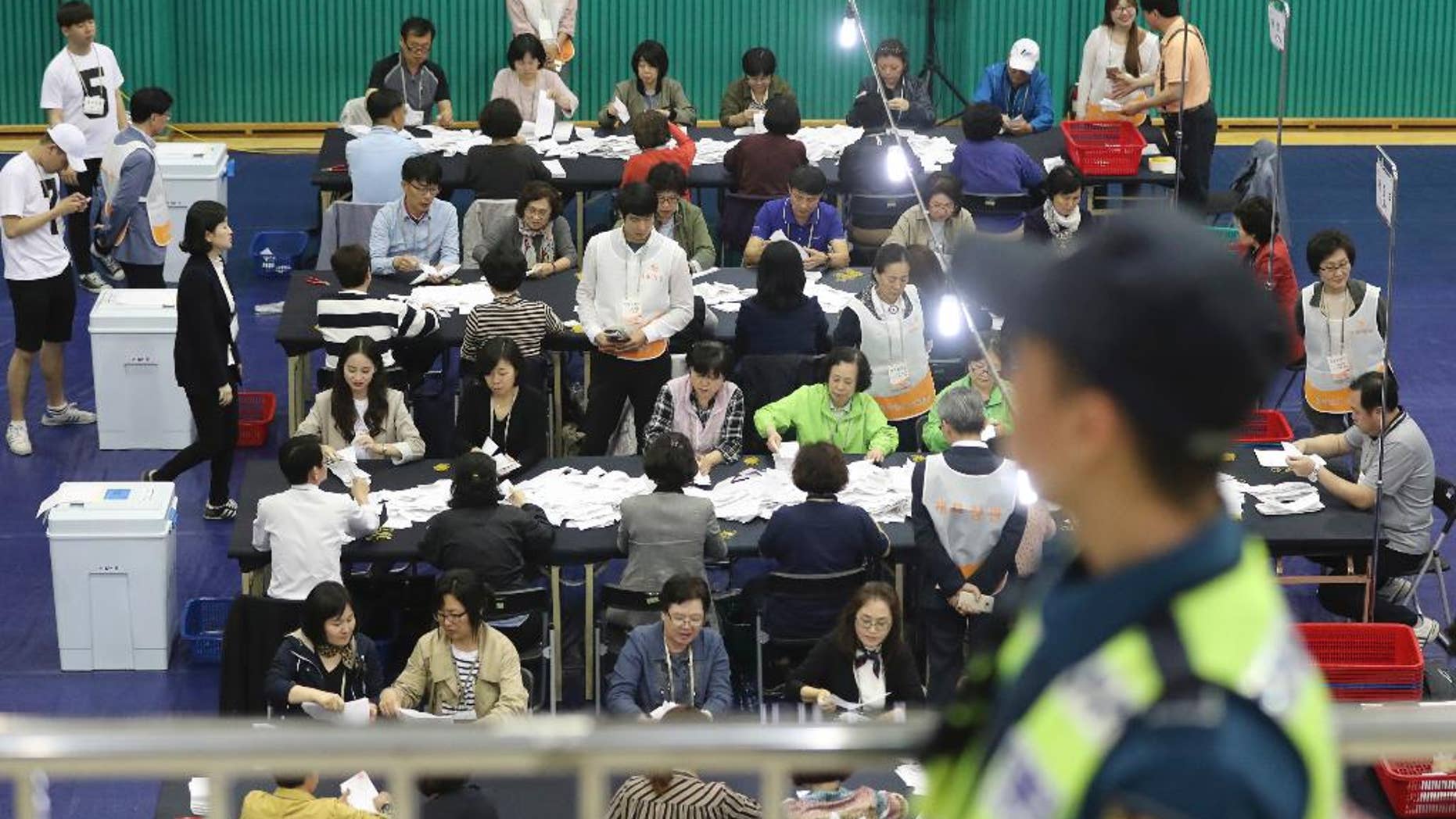 South Korean National Election Commission officials sort out ballots in the country's presidential election as a police officer stand guard in Seoul, South Korea, Tuesday, May 9, 2017. Two major challengers for South Korean president, a conservative and a centrist, conceded defeat Tuesday, paving the way for liberal Moon Jae-in to claim victory in an election that followed months of political turmoil caused by ousted President Park Geun-hye's corruption scandal. (AP Photo/Lee Jin-man)