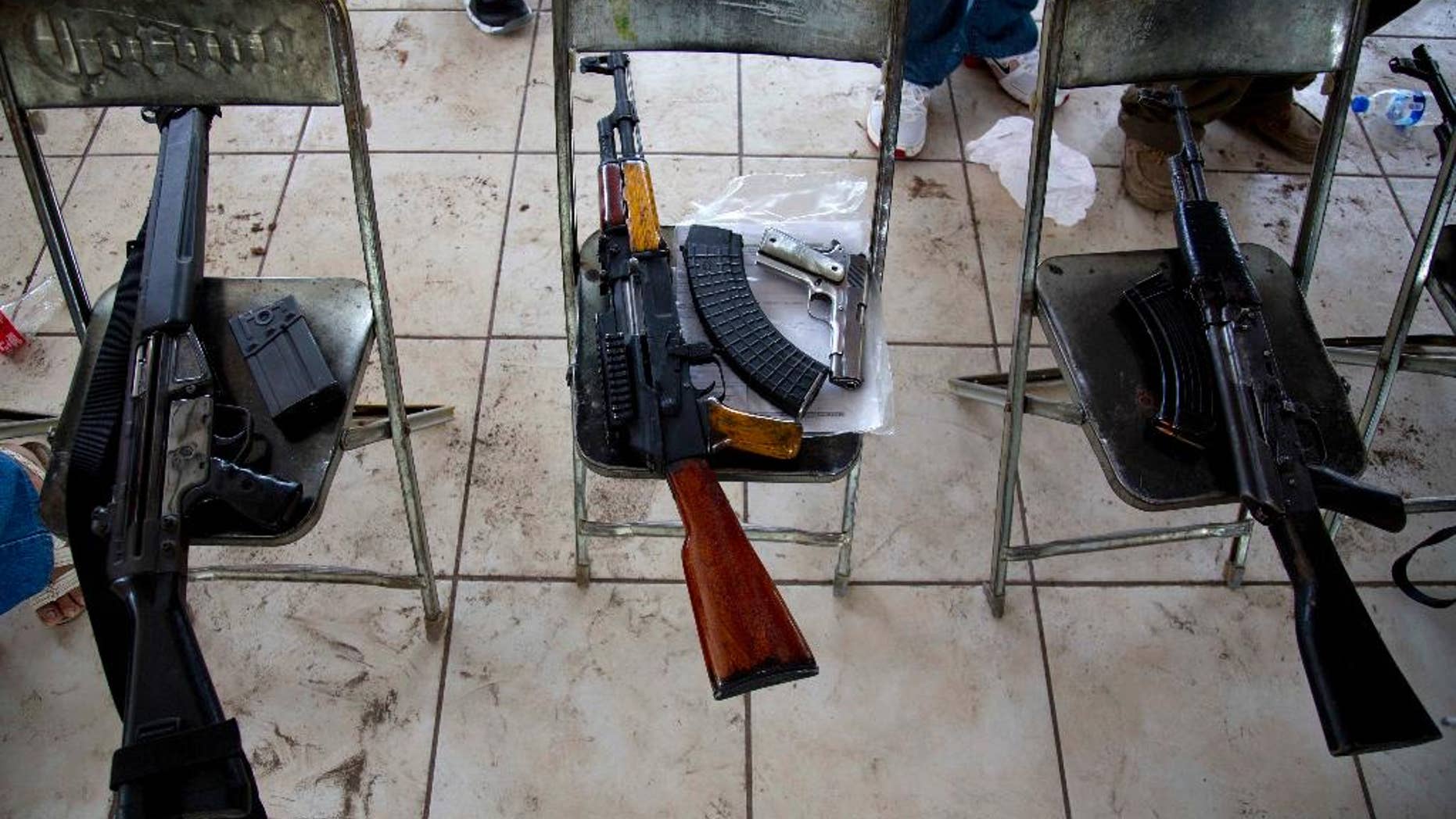 In this May 8, 2014 photo, weapons that belong to members of self-defense groups sit on chairs during a weapons registration operation in Apatzingan, Mexico. The self-defense members, identified by their white T-shirts, have registered thousands of weapons. But they’ve been allowed to keep them, even the large-caliber rifles that under Mexican law can only be used by the military. (AP Photo/Eduardo Verdugo)