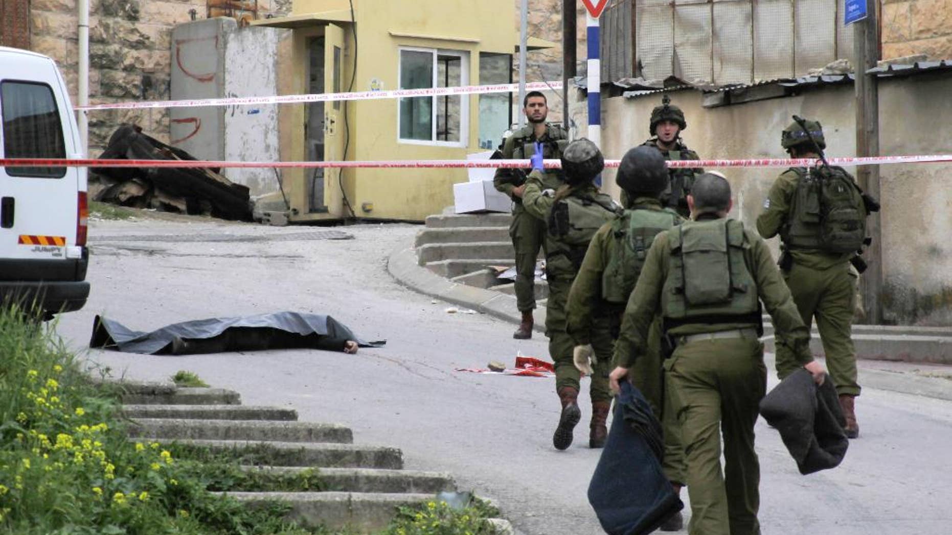 FILE - In this Thursday, March 24, 2016 file photo, Israeli soldiers stand near the body of a Palestinian who was shot and killed by a soldier while laying wounded on the ground after a stabbing attack in Hebron, West Bank. Israeli Prime Minister Benjamin Netanyahu defended the military Sunday, March 27, 2016 following uproar over footage of a soldier lethally shooting a Palestinian attacker who had already been shot and subdued. (AP Photo, File)
