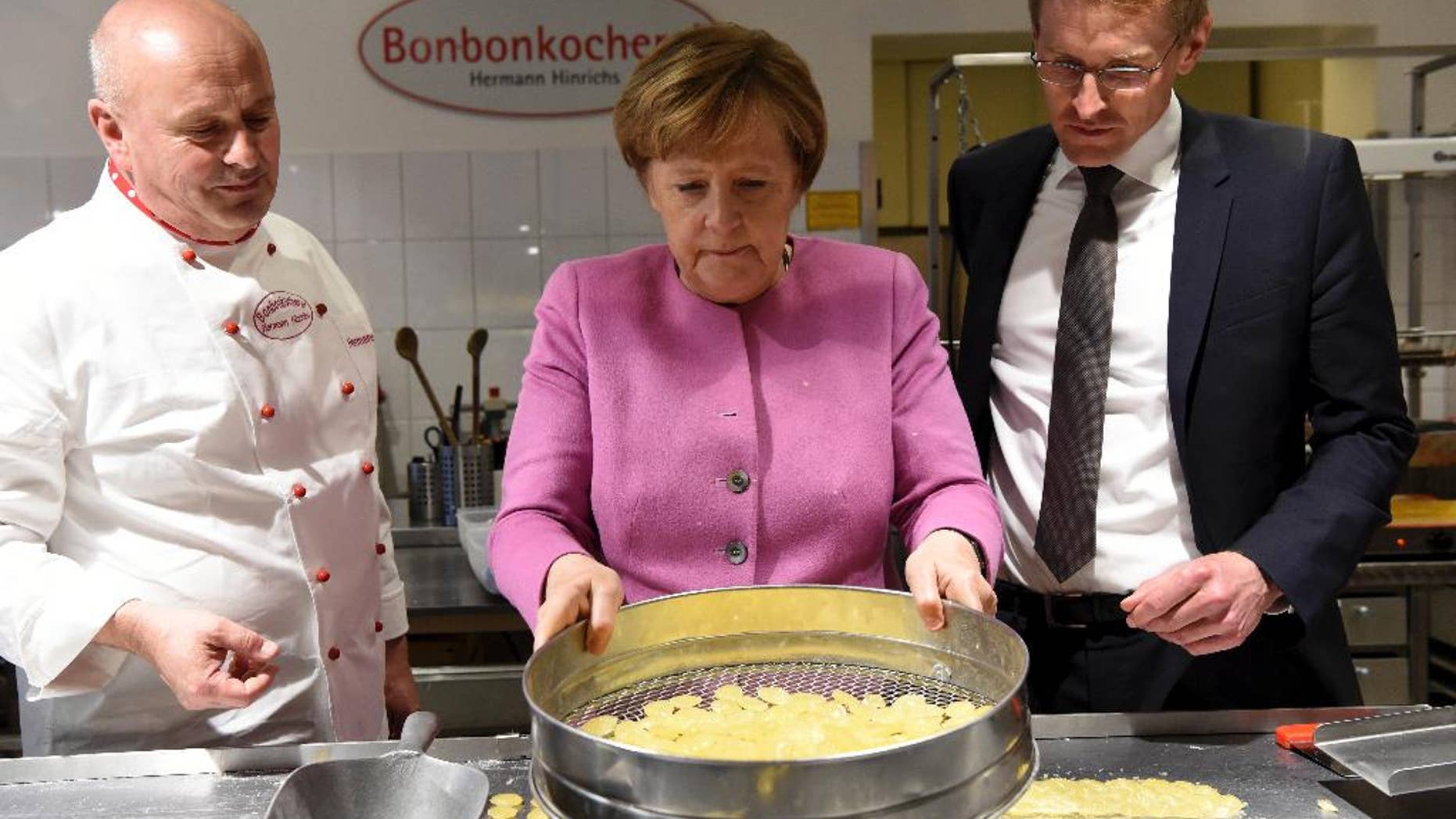 German Chancellor Angela Merkel is flanked by the Christian Democratic party's top candidate for the Schleswig-Holstein stage election Daniel Guenther, right, and the owner Hermann Hinrichs, when visiting a candy cookery in Eckernfoerde, northern Germany, Friday, May 5, 2017, two days before the state elections in Schleswig-Holstein. (Carsten Rehder/dpa via AP)
