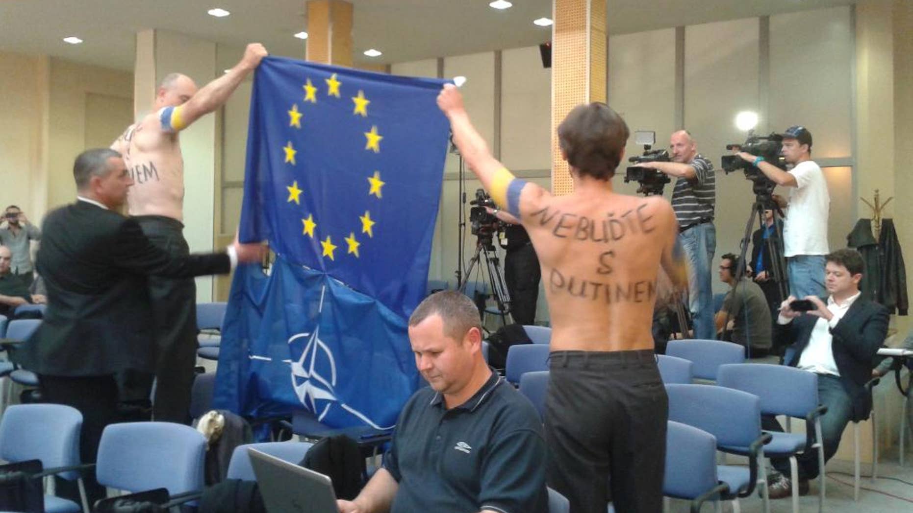 Two men protesting against Czech PM Bohuslav Sobotka and his cabinet´s stance on the Ukrainian crisis disturbed the press conference after the government´s meeting in Prague, Czech Republic, Wednesday, Oct. 8, 2014. The two protesters stripped to the waist called on Sobotka (Social Democrats, CSSD) to defend freedom and not to help Russian President Vladimir Putin. During the press conference, both men were sitting among other journalists at the Government Office. When Sobotka was leaving the conference room earlier over the appointment of the new regional development minister, they took off their upper clothes and stood up to express a silent protest. Letters on the back at right read "Don't side with Putin". (AP Photo/CTK, Sarka Dvorakova)