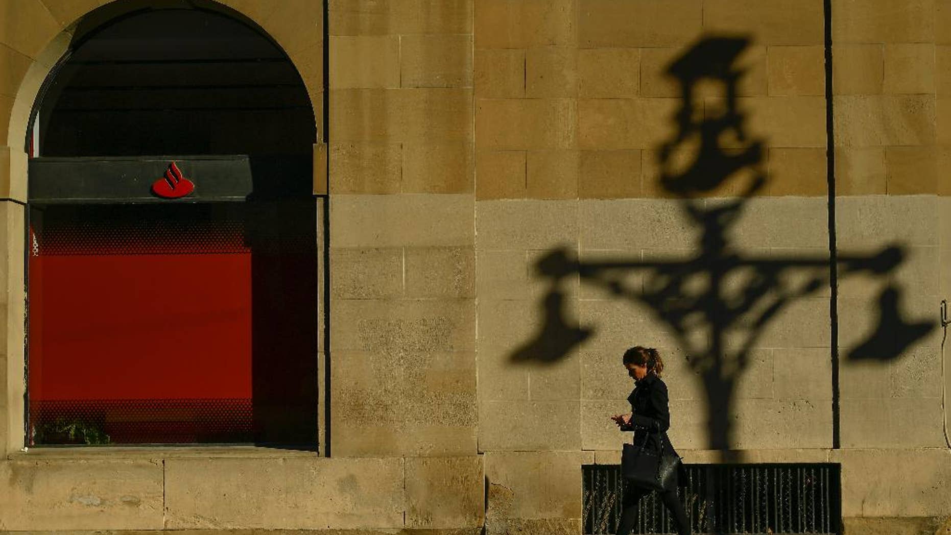 A woman walks past checking her personal phone beside a wall with the shadow of a street light, during an autumn day, in Pamplona northern Spain, Thursday, Dec. 1, 2016. (AP Photo/Alvaro Barrientos)