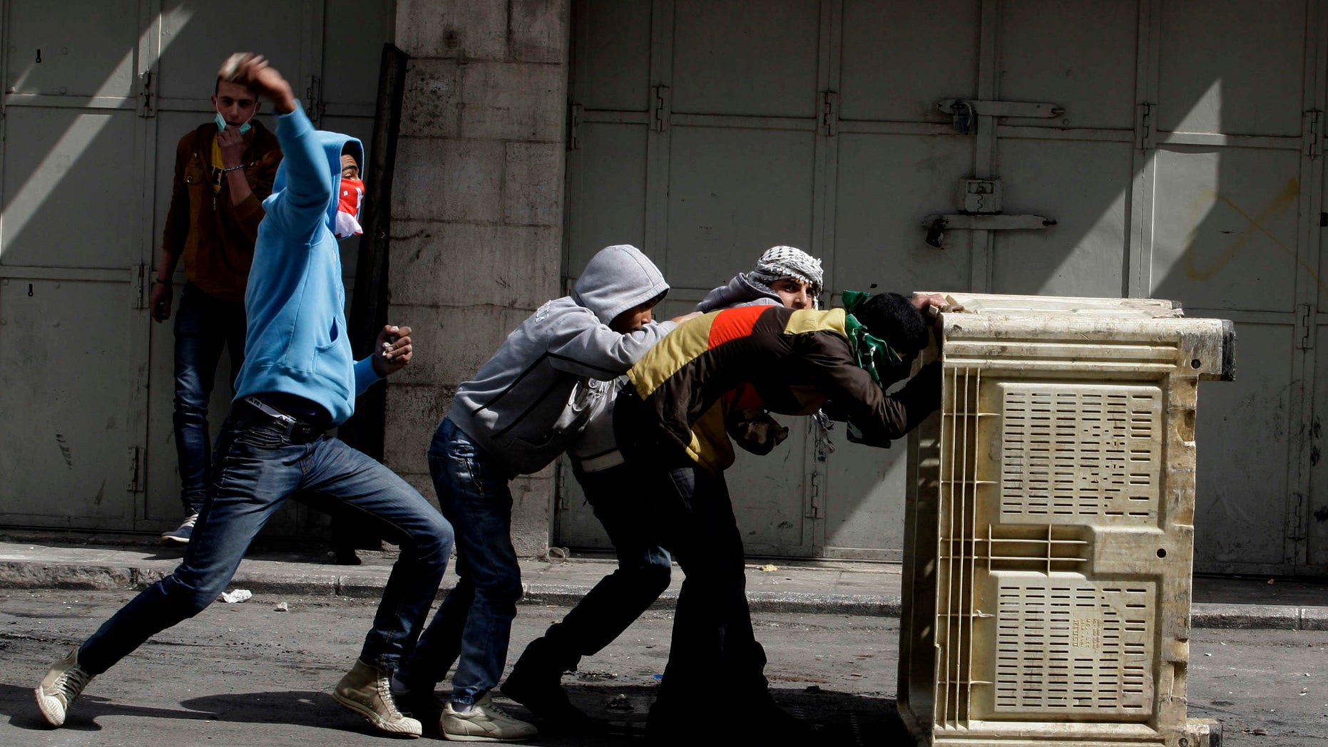 Palestinians take cover during clashes with Israeli troops in the West Bank city of Hebron, following the death of Arafat Jaradat, a Palestinian prisoner held in an Israeli jail, Sunday, Feb. 24, 2013. The death of a 30-year-old Palestinian after interrogation by Israel's Shin Bet security service stokes new West Bank clashes, along with Israeli fears of a third Palestinian uprising. (AP Photo/Nasser Shiyoukhi)