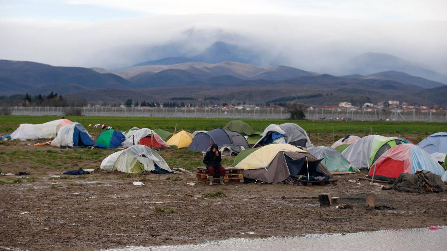 A migrant sits in front of his tent on a windy day in the makeshift refugee camp at the northern Greek border point of Idomeni, Greece, Thursday, March 24, 2016. Conditions in Idomeni, where thousands have been stranded since the border shut to refugees earlier this month, have steadily deteriorated, exacerbated by days of rain that have turned the fields into muddy swamps. (AP Photo/Darko Vojinovic)