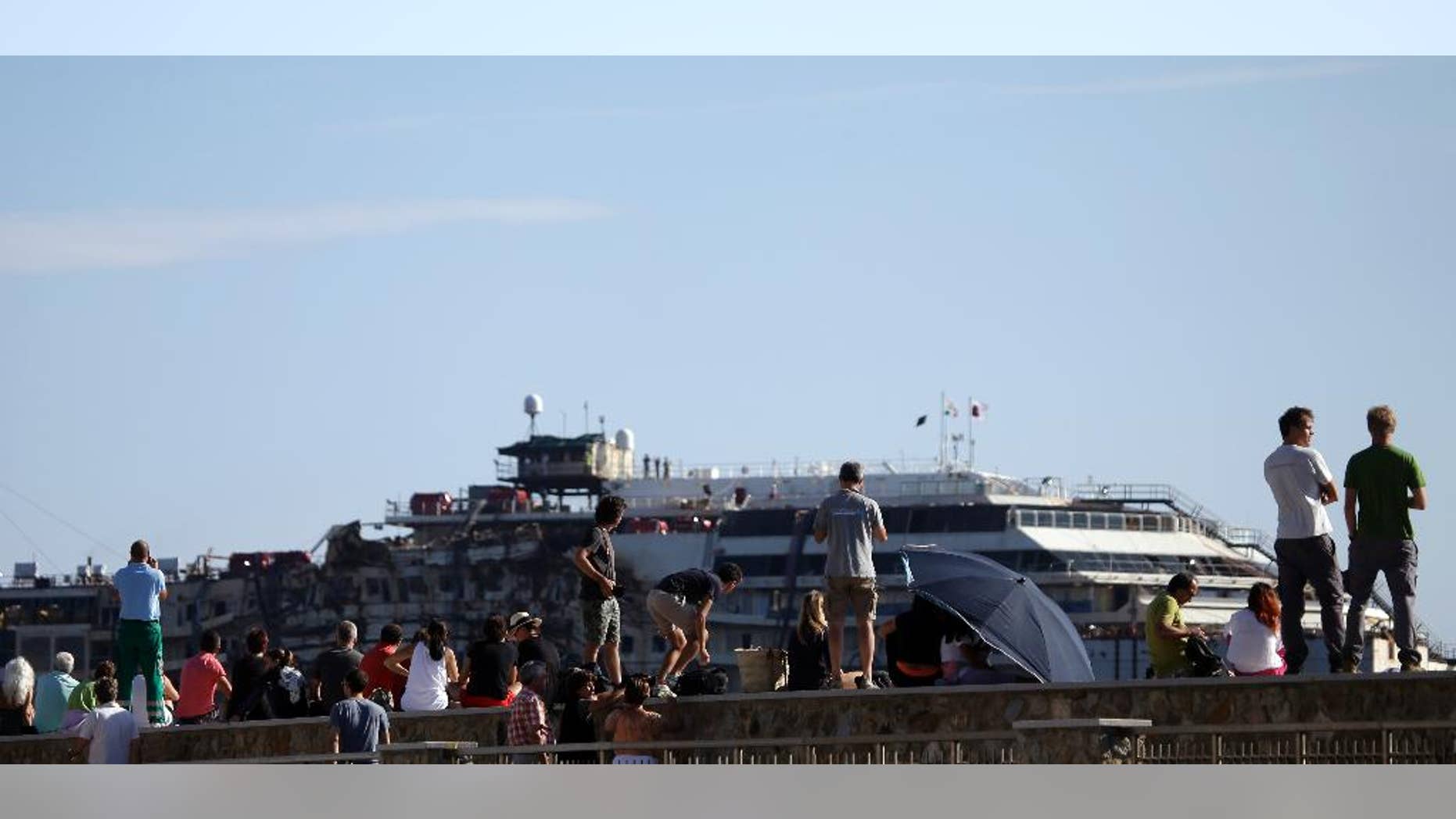 People gather to see the Costa Concordia cruise wreck being towed away from the tiny Tuscan island of Isola del Giglio, Italy, Wednesday, July 23, 2014. After more than two years since it slammed into a reef along the coastline of Isola del Giglio the wreck has begun its last journey, to the Italian port of Genoa, where it will be scrapped. 32 people died in the incident. (AP Photo/Gregorio Borgia)