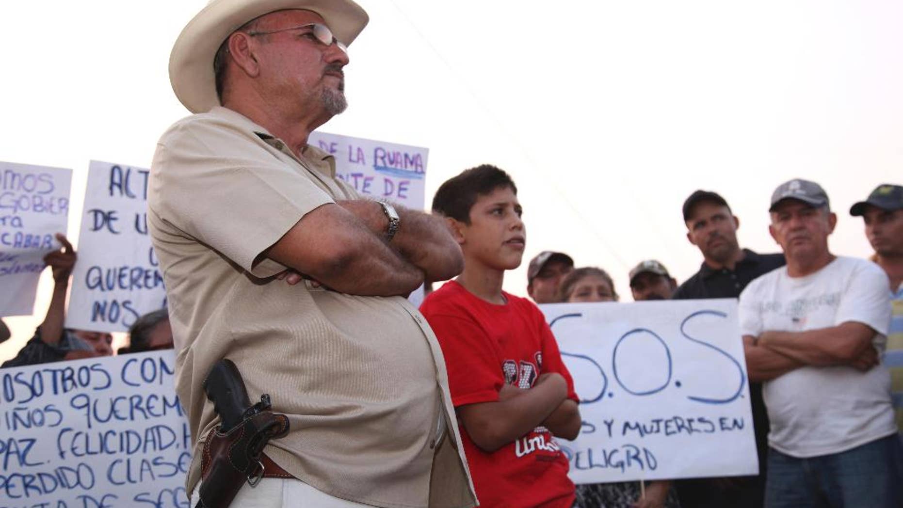 FILE - In this May 19, 2013 file photo, Hipolito Mora, leader of a local self-defense movement, stands with a side-arm as residents protest extortion fees and kidnappings by the Knights of Templar drug cartel in La Ruana, Mexico. On Dec. 16, 2014, Mora’s group had a deadly shootout with a rival rural police force led by Luis Antonio Torres, better known as "Simon the American," that left 11 people dead, including Mora's son, in the remote mountain town of La Ruana, Michoacan. On Saturday, Jan. 3, 2015, a judge said there was sufficient evidence against Mora and his followers of involvement in 10 homicides during the shootout to merit the launch of homicide proceedings. (AP Photo/Marco Ugarte, File)