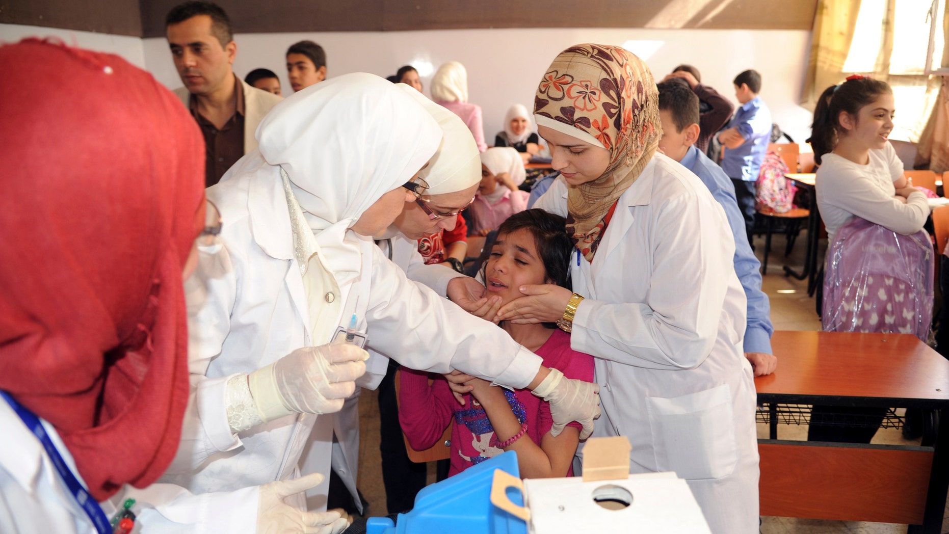 Syrian health workers administer polio vaccination to a girl at a school in Damascus. (REUTERS/SANA/Handout via Reuters)