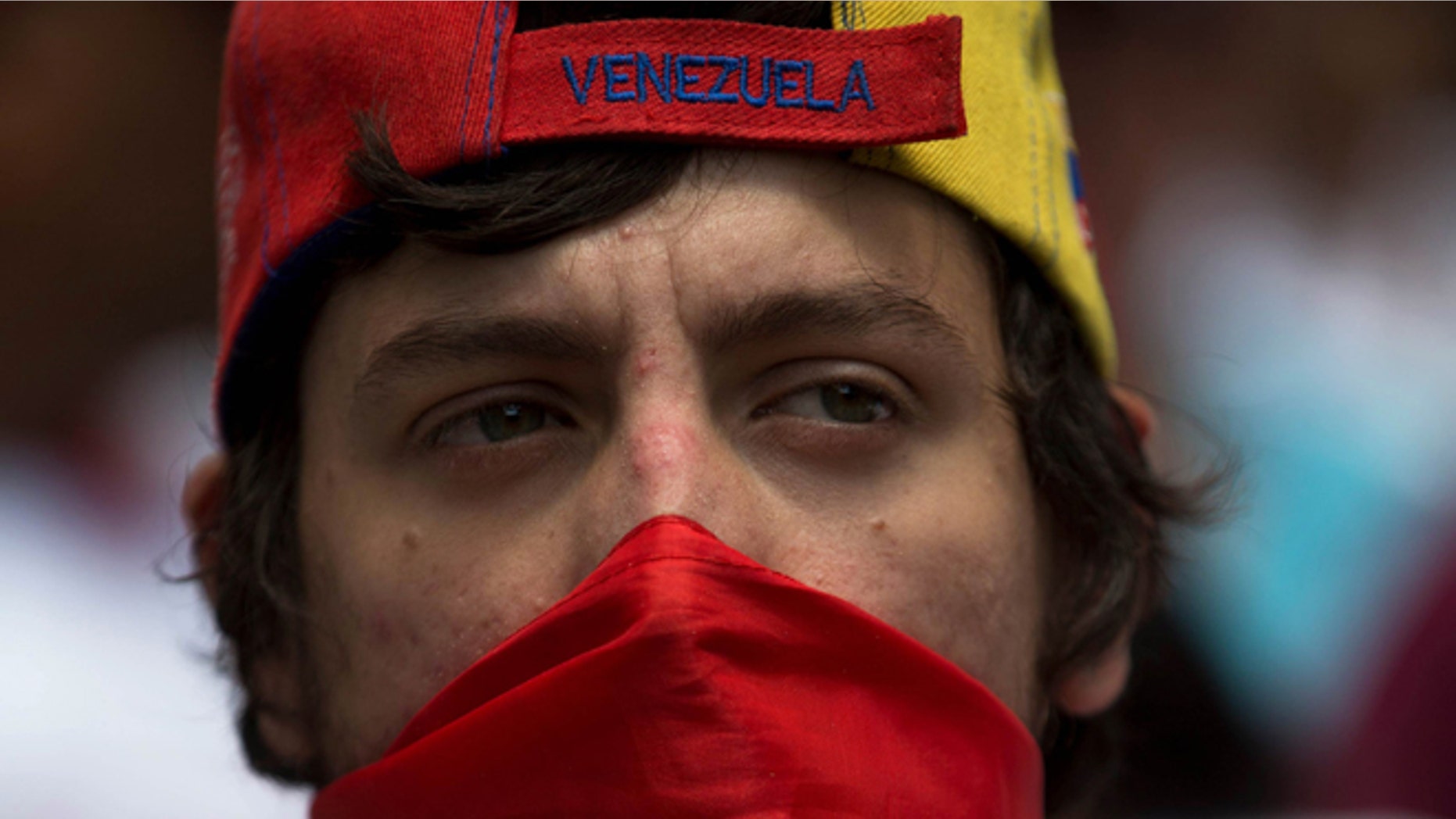 An opposition member covers his face with a Venezuelan flag during a protest in Caracas, Venezuela, Saturday, Feb. 28, 2015. Marchers are taking to the streets of Caracas in dueling protests, with one group calling attention to a crackdown on opponents of the government and another showing support for the embattled socialist administration.(AP Photo/Fernando Llano)