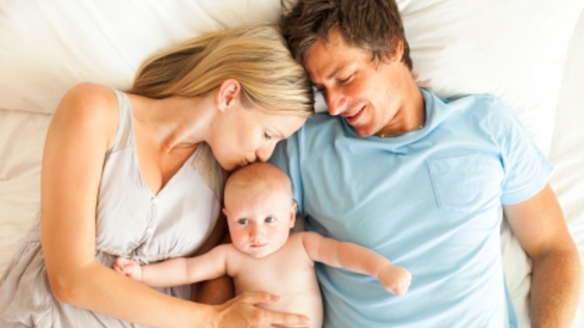 Caring parents with baby lying in bed. Horizontal Shot.