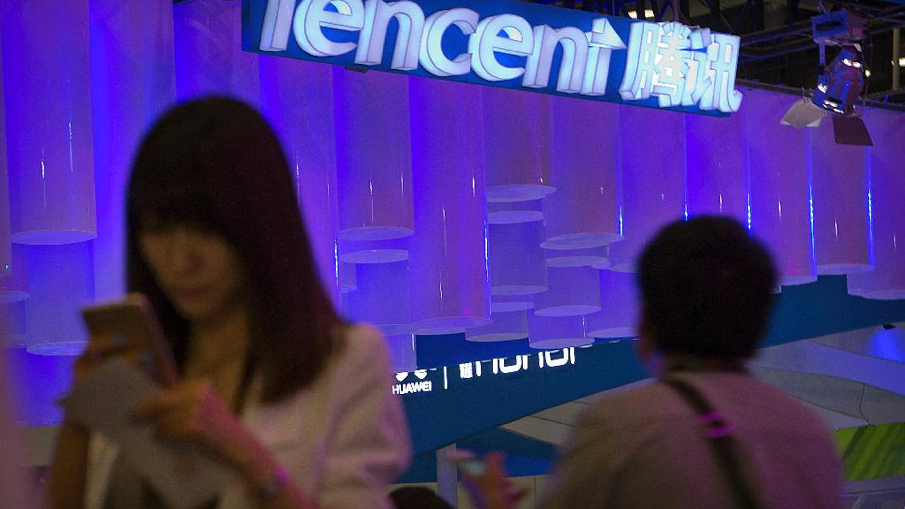 In this April 29, 2015 photo, a woman uses her smartphone near a booth for the Chinese Internet company Tencent at the Global Mobile Internet Conference in Beijing. Chinese state media reported Thursday, Aug. 18, 2016, that new rules hold chief editors of news websites personally liable for content, months after several portals posted material that was seen as embarrassing to President Xi Jinping. Tencent, one of China's most popular websites, fired its top editor after a July headline mistakenly said Xi delivered a "furious" - instead of "important" - speech commemorating a Communist Party anniversary. (AP Photo/Mark Schiefelbein)
