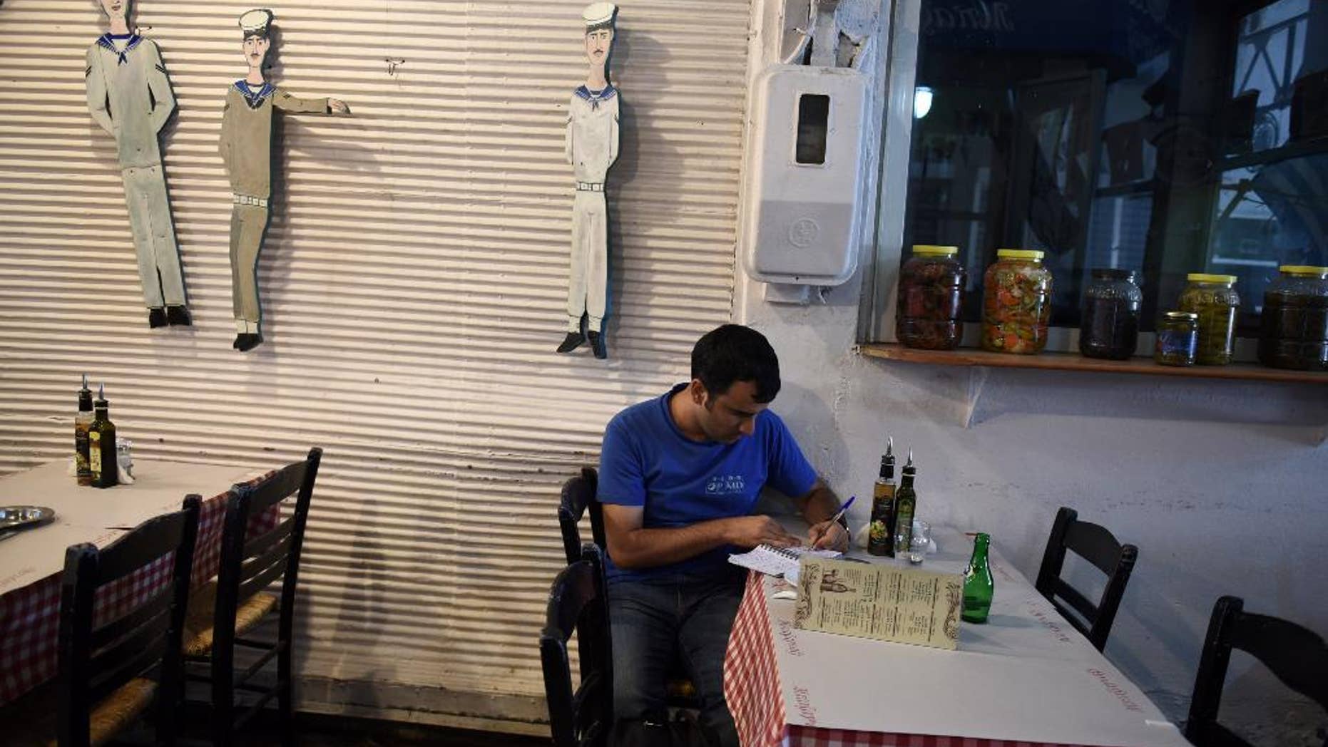 A restaurant employee writes on a paper at the northern Greek port city of Thessaloniki, Tuesday, Aug. 11, 2015. Greece has agreed on the broad terms of a new three-year bailout package with international creditors, with only a few details left to iron out, the finance minister said Tuesday.(AP Photo/Giannis Papanikos)
