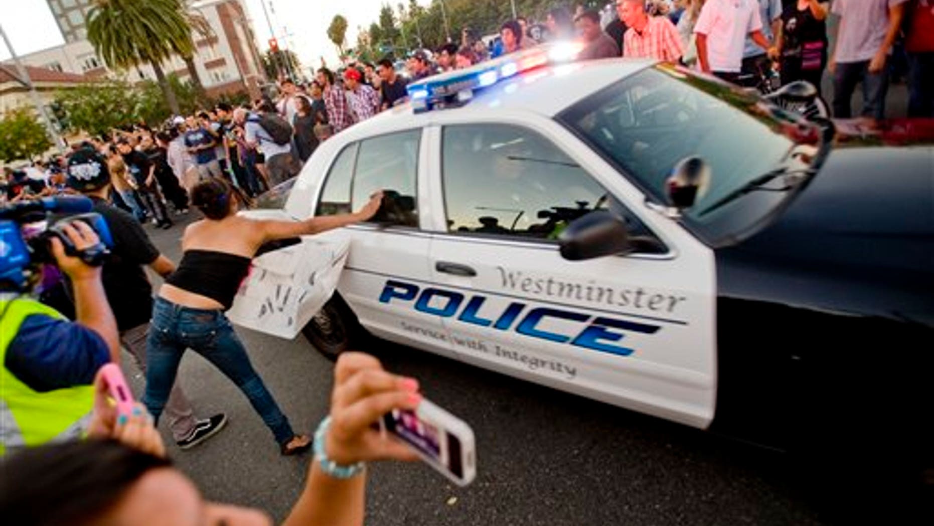Protesters hit police cars as they drive by the intersection of Broadway and Anaheim Blvd Tuesday night JKuly 25, 2012 as police attempt to regroup to put down the disturbance. Back-to-back weekend shootings by police have sparked four days of protests. (AP Photo/The Orange County Register,Paul Rodriguez ) MAGS OUT; LOS ANGELES TIMES OUT