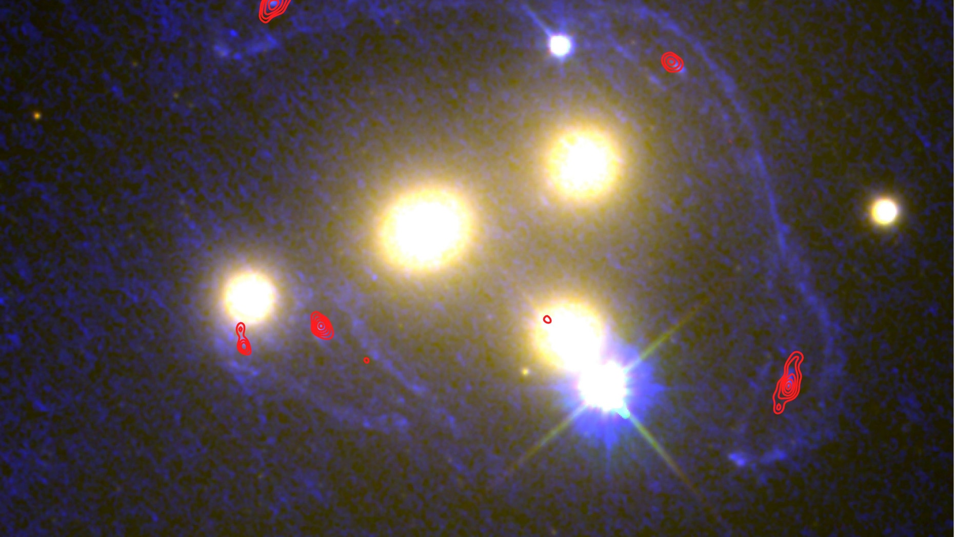 This image shows the four central galaxies in the Abell 3827 cluster with ultraviolet light from the Hubble images (blue) and infrared light from the ALMA observations (red). At these wavelengths, scientists can determine the extent to which a galaxy behind the cluster has been distorted by the gravity of the normal and dark matter.