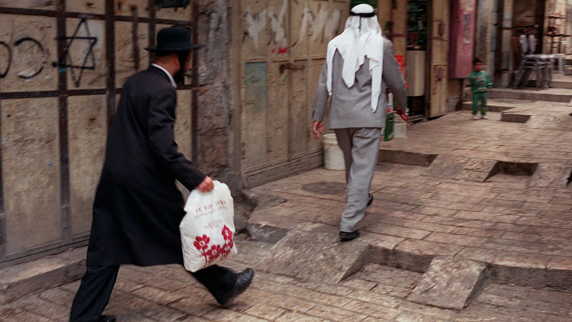 FOR STORY ISRAEL NATION : In this June 12, 1997 file photo, an Orthodox man walks behind a Palestinian man on a street in the walled Old City of Jerusalem. Israel's national population registry lists many “nationalities” and ethnicities, among them Jew, Arab, Druze and more, but one ethnicity is conspicuously absent from the list: Israeli. The Israeli Supreme Court ruled this week that residents cannot identify themselves as Israelis in the national registry because it could affect the country’s Jewish character, in court documents obtained Thursday, Oct, 3, 2013. (AP Photo/Greg Marinovich, File)