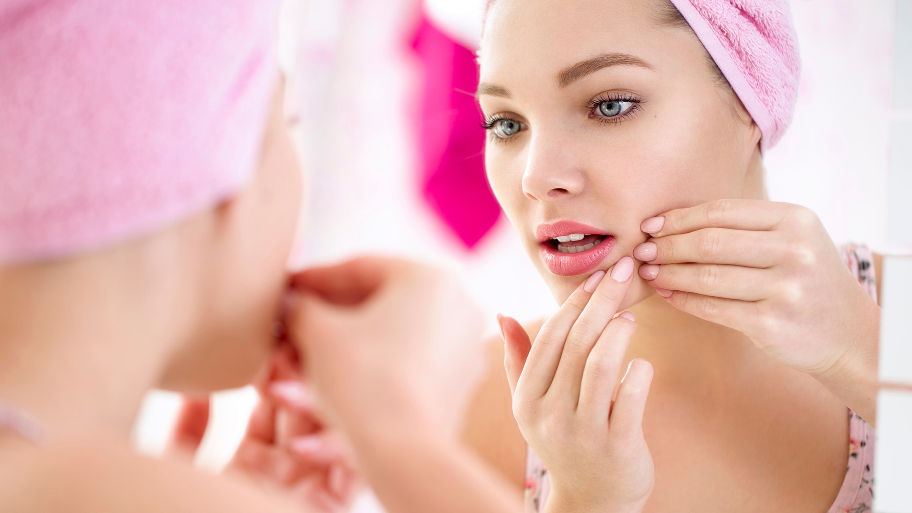 Young teenage girl looking pimple on her face in a mirror, concept problem on skin