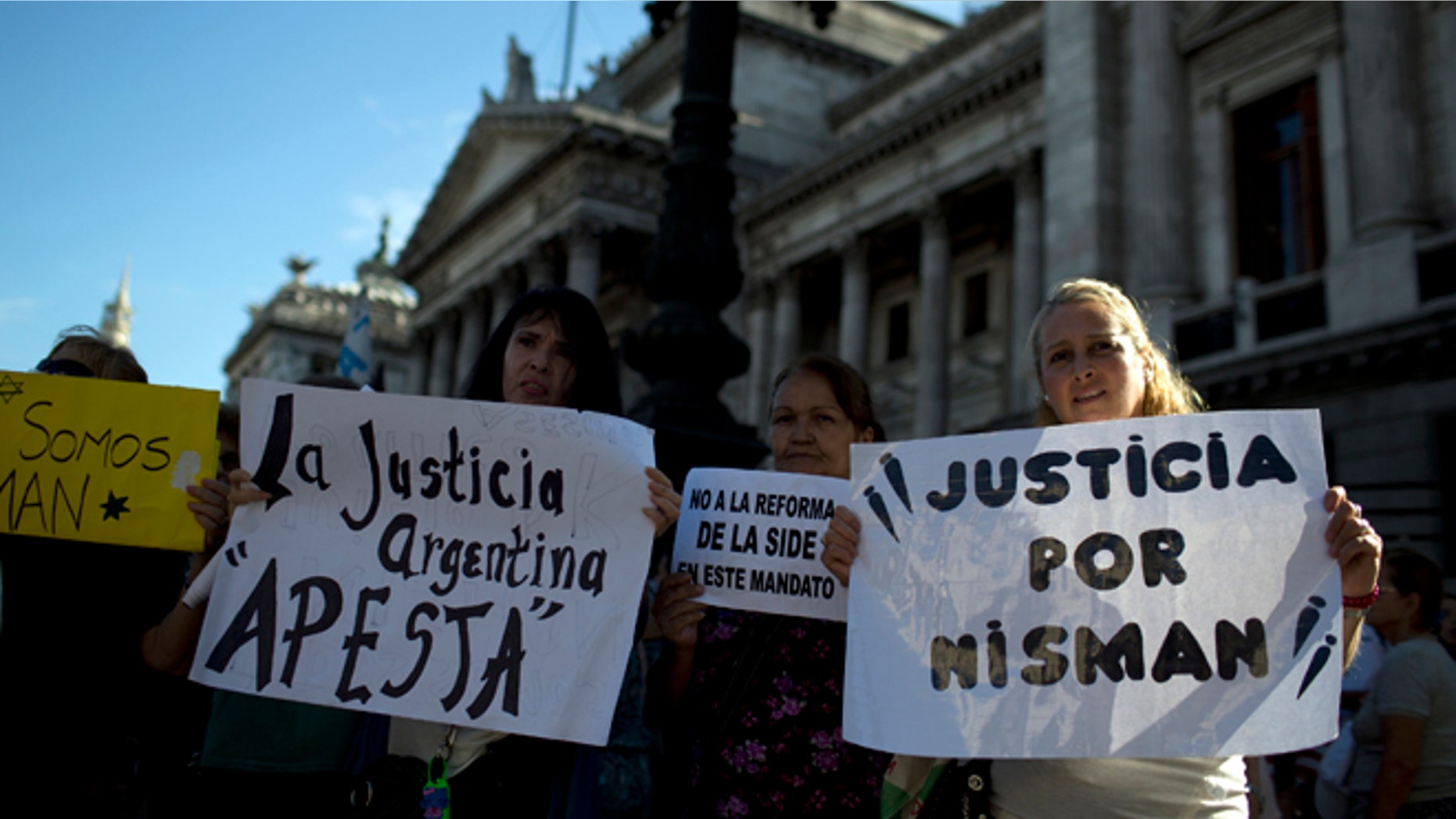 Women holds sign that reads in Spanish; "Argentine justice stinks," second left, "and "Justice for Nisman," right, during a march for justice and against impunity in the case of the mysterious death of late prosecutor Alberto Nisman, in Buenos Aires, Argentina, Wednesday, Feb. 4, 2015. Investigators examining the death of Nisman, who accused Argentine President Cristina Fernandez of agreeing to shield the alleged masterminds of a 1994 terror bombing, said Tuesday, they have found a draft document he wrote requesting her arrest. (AP Photo/Rodrigo Abd)