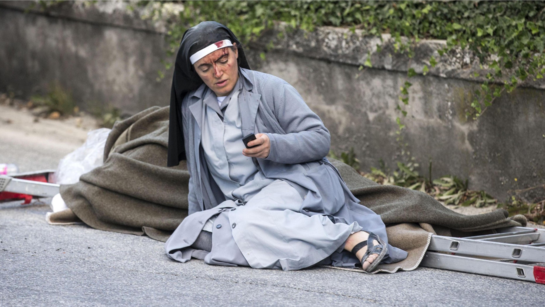 Aug. 24, 2016: Sister Marjana, from Albania, checks her mobile phone as she lies near a victim laid on a ladder following an earthquake in Amatrice, Italy.