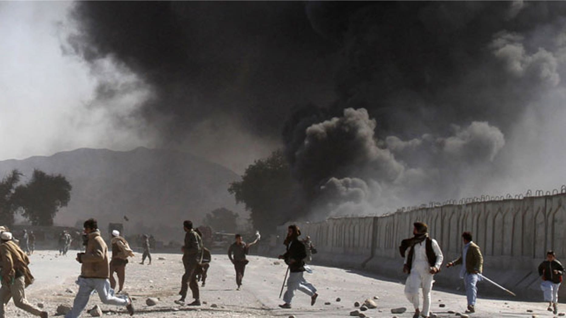 In this Feb. 22, 2012 file photo, protestors run as smoke rises from burning trucks during an anti-U.S. demonstration at a NATO military base in Jalalabad east of Kabul, Afghanistan.