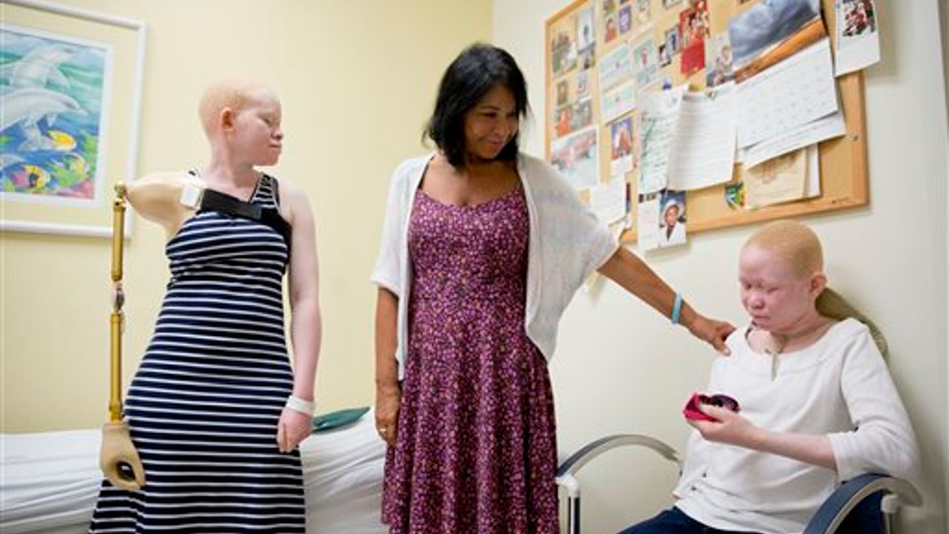 Elissa Montanti, founder and director of the Global Medical Relief Fund, center, places a hand on Pendo Sengerema Noni, right, as Kabula Nkarango Masanja, left, looks on during a prosthetic limb fitting, Tuesday, Aug. 25, 2015, at Shriners Hospital for Children in Philadelphia. (AP Photo/Matt Rourke)