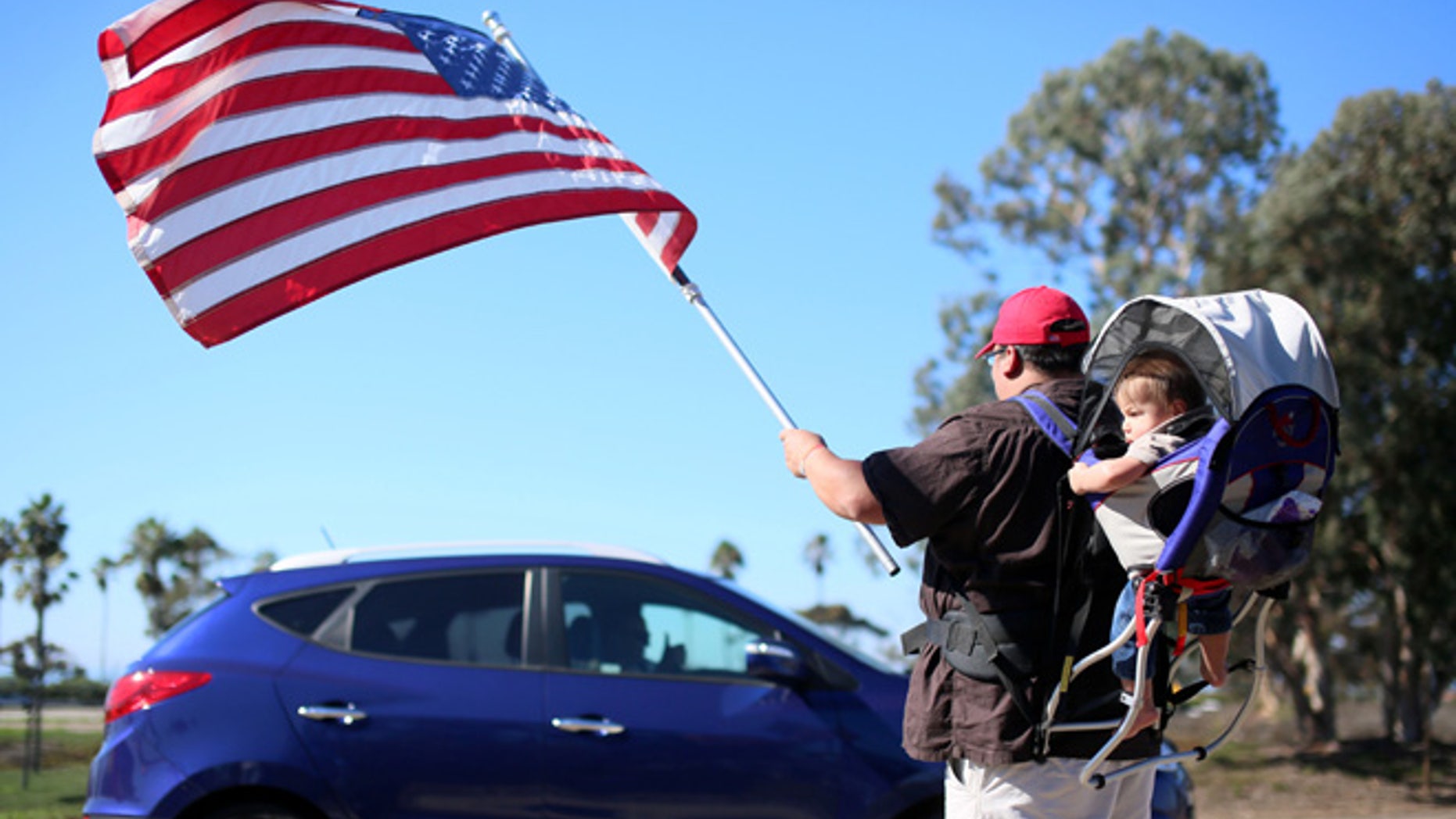 Demonstrator Steven Morales with his son Steven Jr. waves an American flag for motorists in support of President elect Donald Trump outside of Camp Pendleton in Oceanside, California, U.S. November 11, 2016. REUTERS/Sandy Huffaker - RTX2TA95