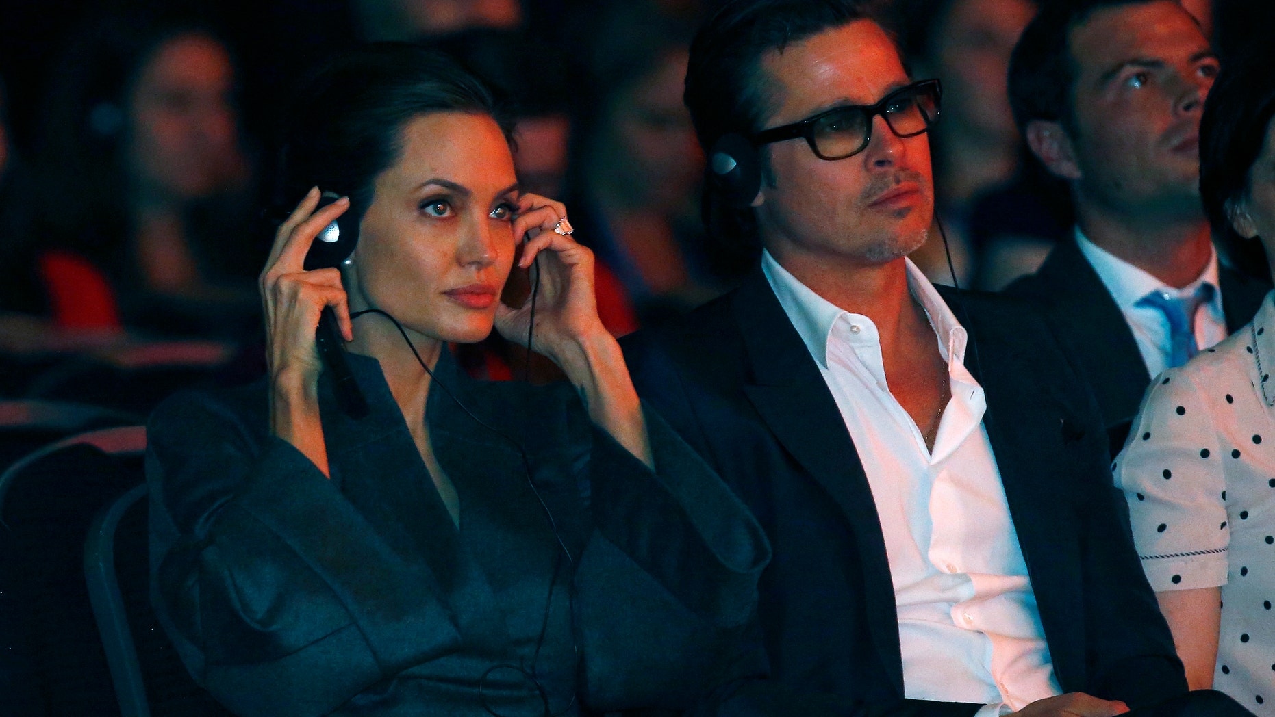 Actress and campaigner Angelina Jolie and her partner Brad Pitt wear headphones to listen to a translation during a global summit on ending sexual violence in conflict, at the ExCel Centre in London June 13, 2014. REUTERS/Luke MacGregor (BRITAIN - Tags: POLITICS ENTERTAINMENT) - RTR3TMBJ