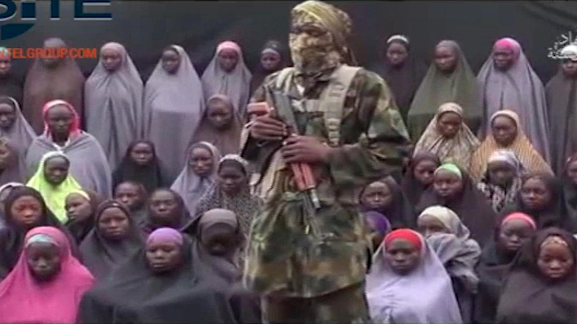 An alleged Boko Haram soldier stands in front of a group of girls alleged to be some of the 276 abducted Chibok schoolgirls held since April 2014, in an unknown location, in video distributed in August 2016.