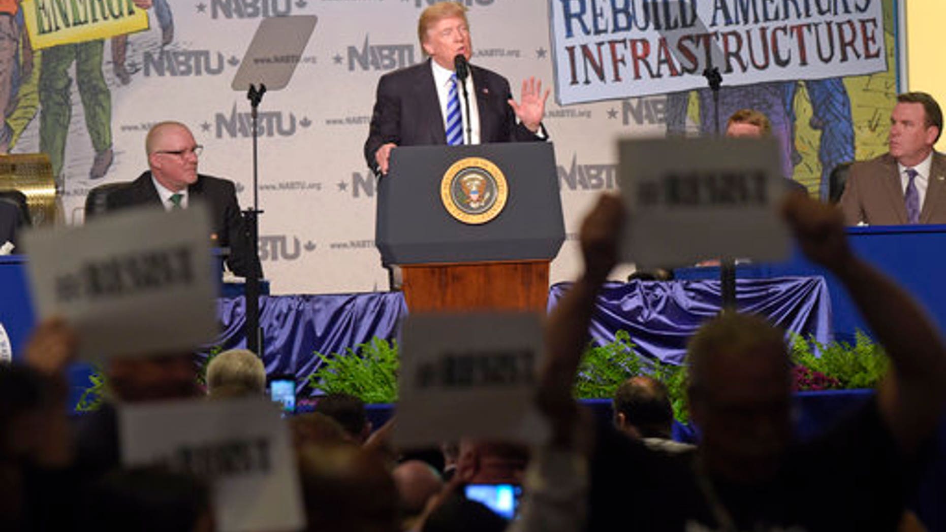 Protesters hold up signs as President Donald Trump speaks at the 2017 North America's Building Trades Unions National Legislative Conference in Washington, Tuesday, April 4, 2017. (AP Photo/Susan Walsh)