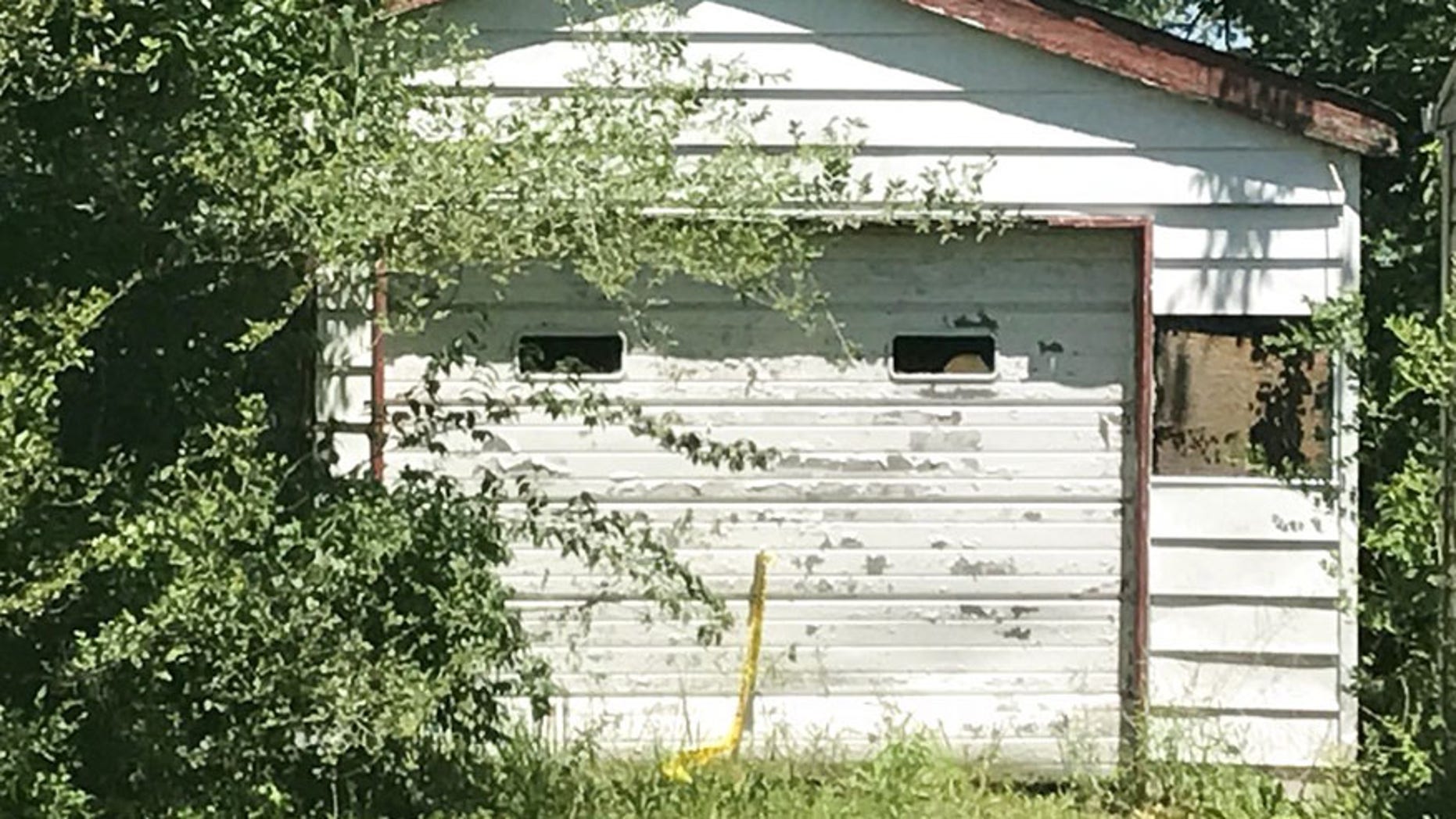 Trees grow in front of the entrance of a garage Tuesday, June 6, 2017, where the remains of a 7-year-old child was found in Centreville, Ill. A Las Vegas woman told investigators Tuesday that her dead child had been in a southern Illinois home for two years, and authorities later found human remains in the vacant house, according to authorities. Centreville police Sgt. DeMarius Thomas Sr. told the St. Louis Post-Disaptch that police believe the child was killed in nearby Belleville, Ill, and dumped in the garage. (Christine Byers/St. Louis Post-Dispatch via AP)