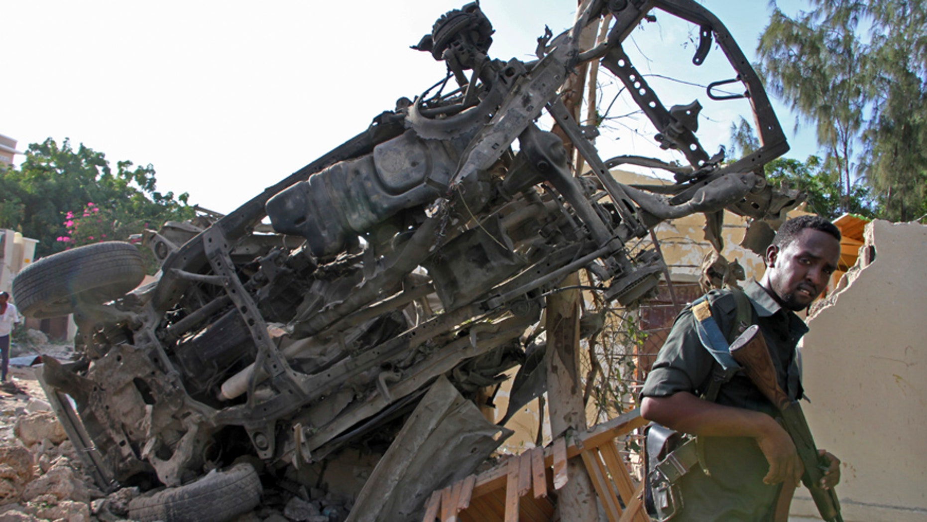 A Somali soldier stands near the wreckage from a car bomb blast and gun battle targeting a restaurant in Mogadishu, Somalia, Thursday, June 15, 2017. Somalia's security forces early Thursday morning ended a night-long siege by al-Shabab Islamic extremists at the popular "Pizza House" restaurant in the capital. (AP Photo/Farah Abdi Warsameh)