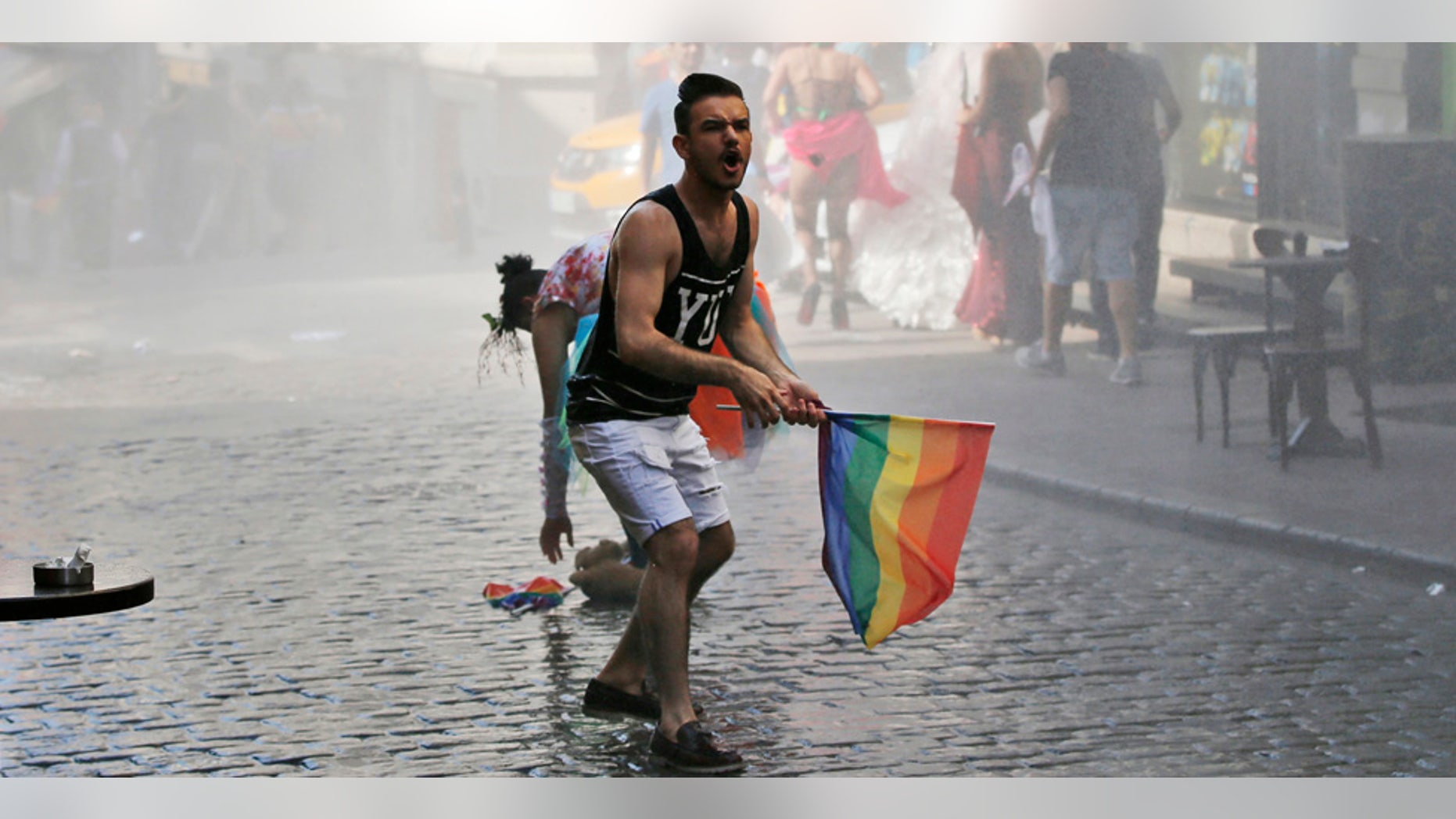 FILE - In this Sunday, June 28, 2015 file photo, a participant of the Pride Week march in Istanbul, reacts as others flee after Turkish police use a water canon to disperse them. For several years, Pride Week in Istanbul attracted tens of thousands of participants, making it one of largest gatherings celebrating gay, lesbian and transgender rights and diversity in the Muslim world. That changed suddenly in 2015, when authorities, citing security concerns, banned gay and trans-gender pride events chasing away shocked participants trying to converge on central Taksim Square with tear gas and water cannons. (AP Photo/Emrah Gurel, File)