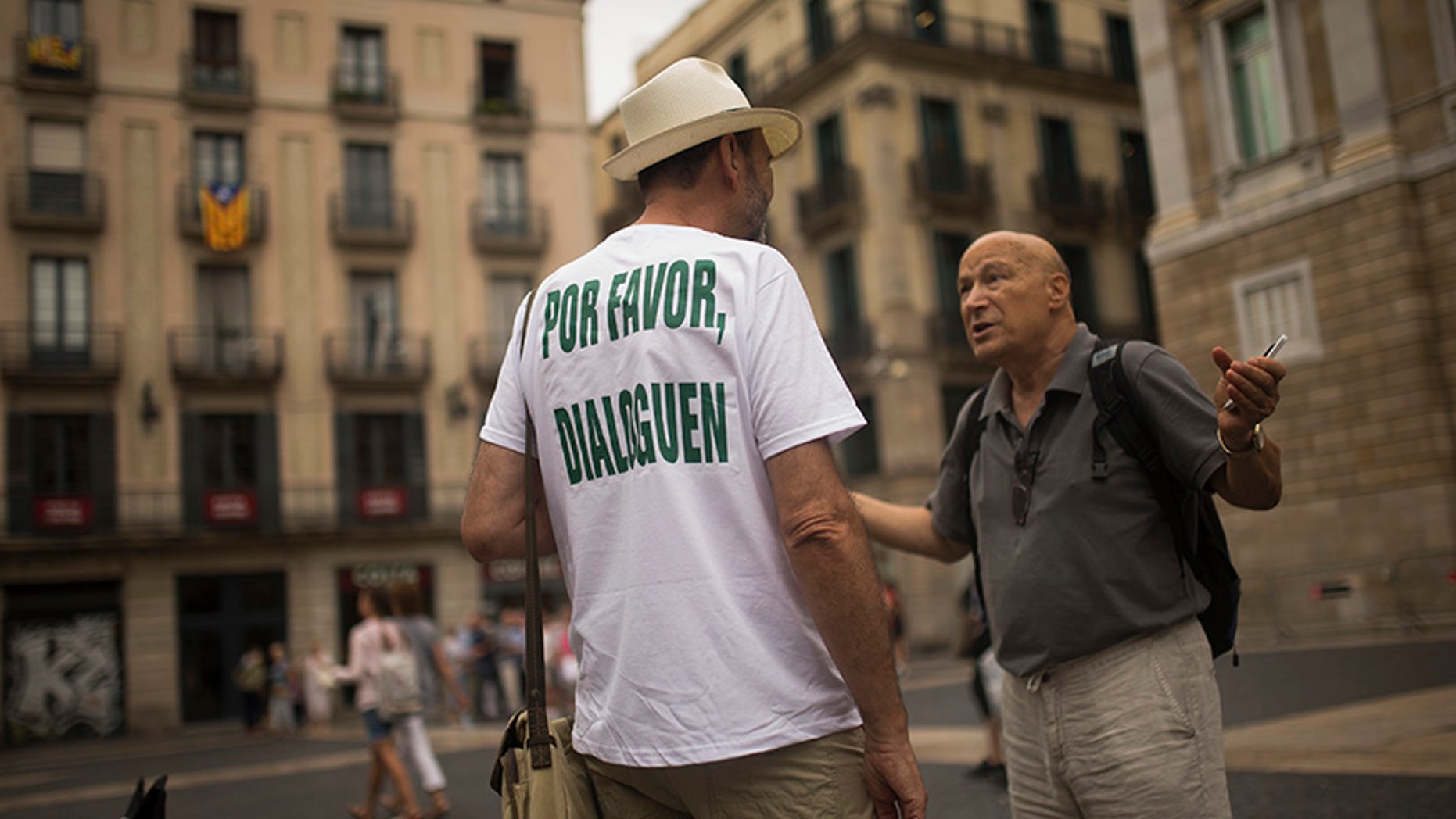 A man, wearing a t-shirt reading in Spanish: "Please, talk" chats with a passer-by about the current political situation in Catalonia, in Barcelona, Friday, Oct. 6, 2017