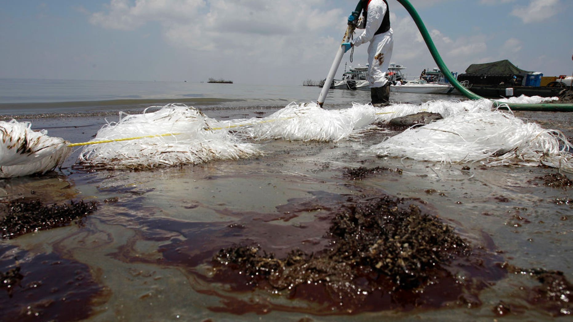A worker uses a suction hose to remove oil washed ashore from the Deepwater Horizon spill, in Belle Terre, La., June 9, 2010.