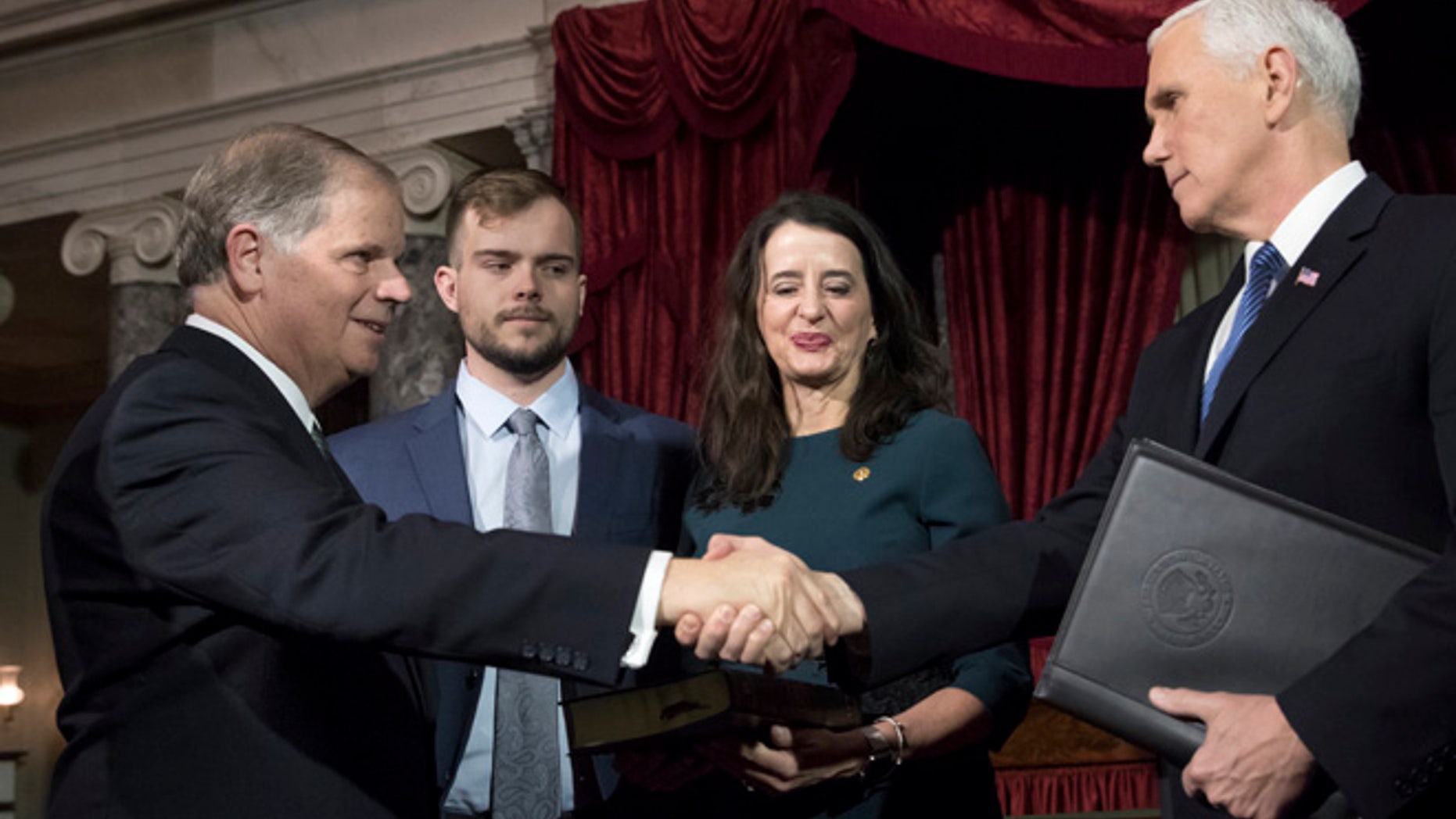 Vice President Mike Pence, right, shakes hands with Sen. Doug Jones, D-Ala., left, after administering the Senate oath of office during a mock swearing in ceremony in the Old Senate Chamber to Jones, with his wife Louise Jones, second from right, Wednesday, Jan. 3, 2018 on Capitol Hill in Washington.