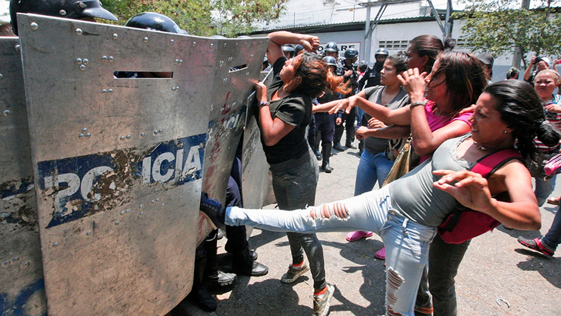 A woman kicks at a riot police shield as relatives of prisoners wait to hear news about their family members imprisoned at a police station where a riot broke out, in Valencia, Venezuela.
