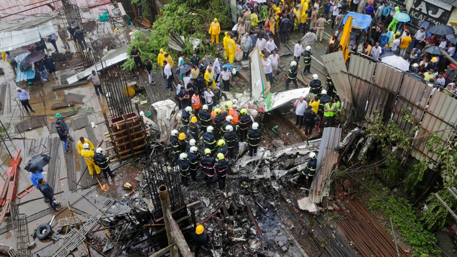 In this June 28, 2018 photo, rescuers stand amid the wreckage of a private chartered plane that crashed in Ghatkopar area, Mumbai, India.