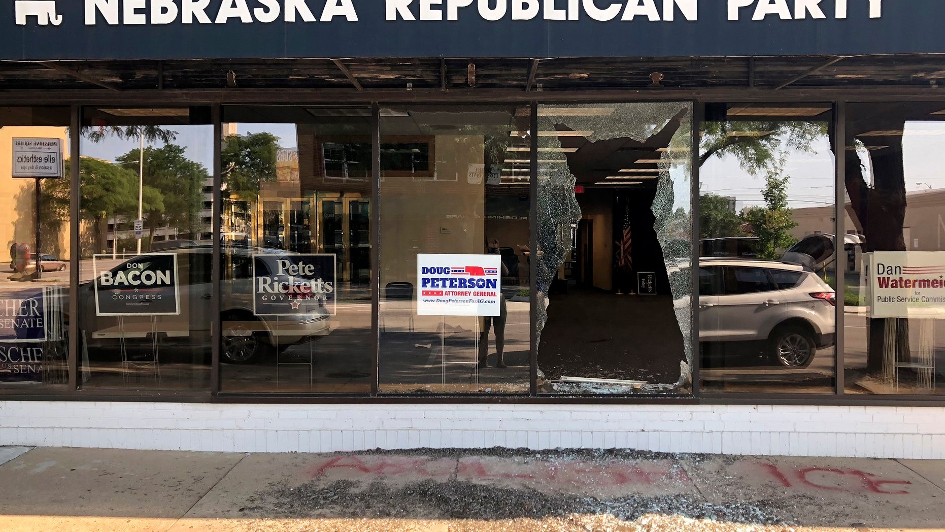 A broken window greets passers-by outside the Nebraska Republican Party's office in Lincoln, Neb., on Tuesday, July 3, 2018. Vandals threw a brick through the window overnight and scrawled the words "Abolish ICE" on the sidewalk below it.